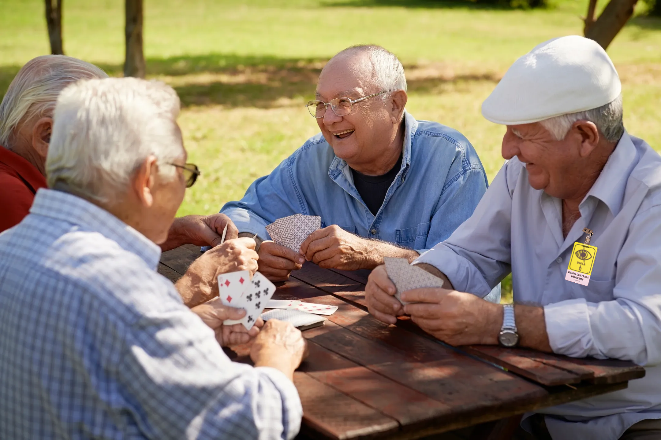 Un groupe de seniors jouent aux cartes en plein air, souriant et profitant du soleil dans un parc.