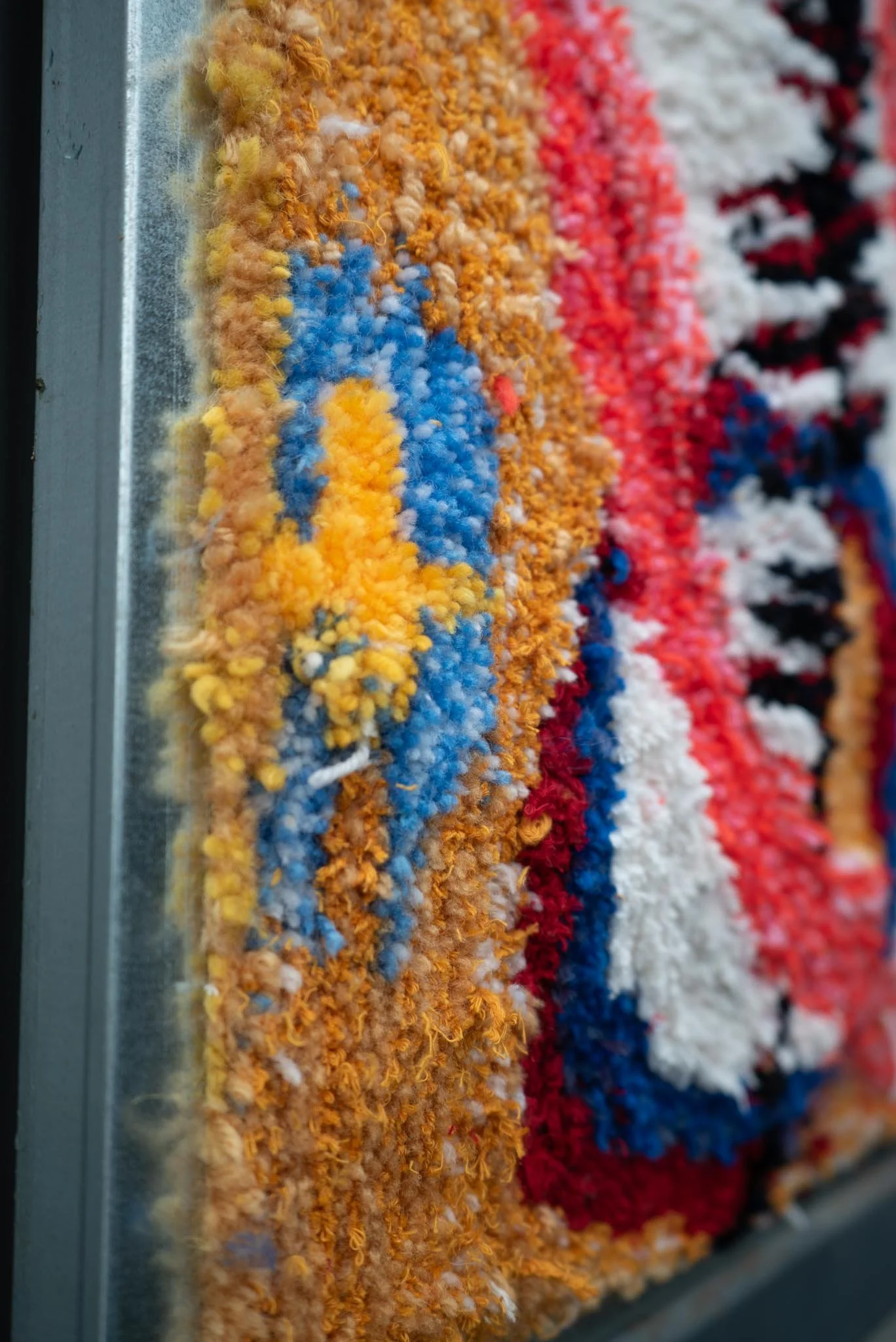 Close-up of a colorful woven rug or textile with various colors including yellow, blue, orange, red, black, and white, displayed on a metallic surface.