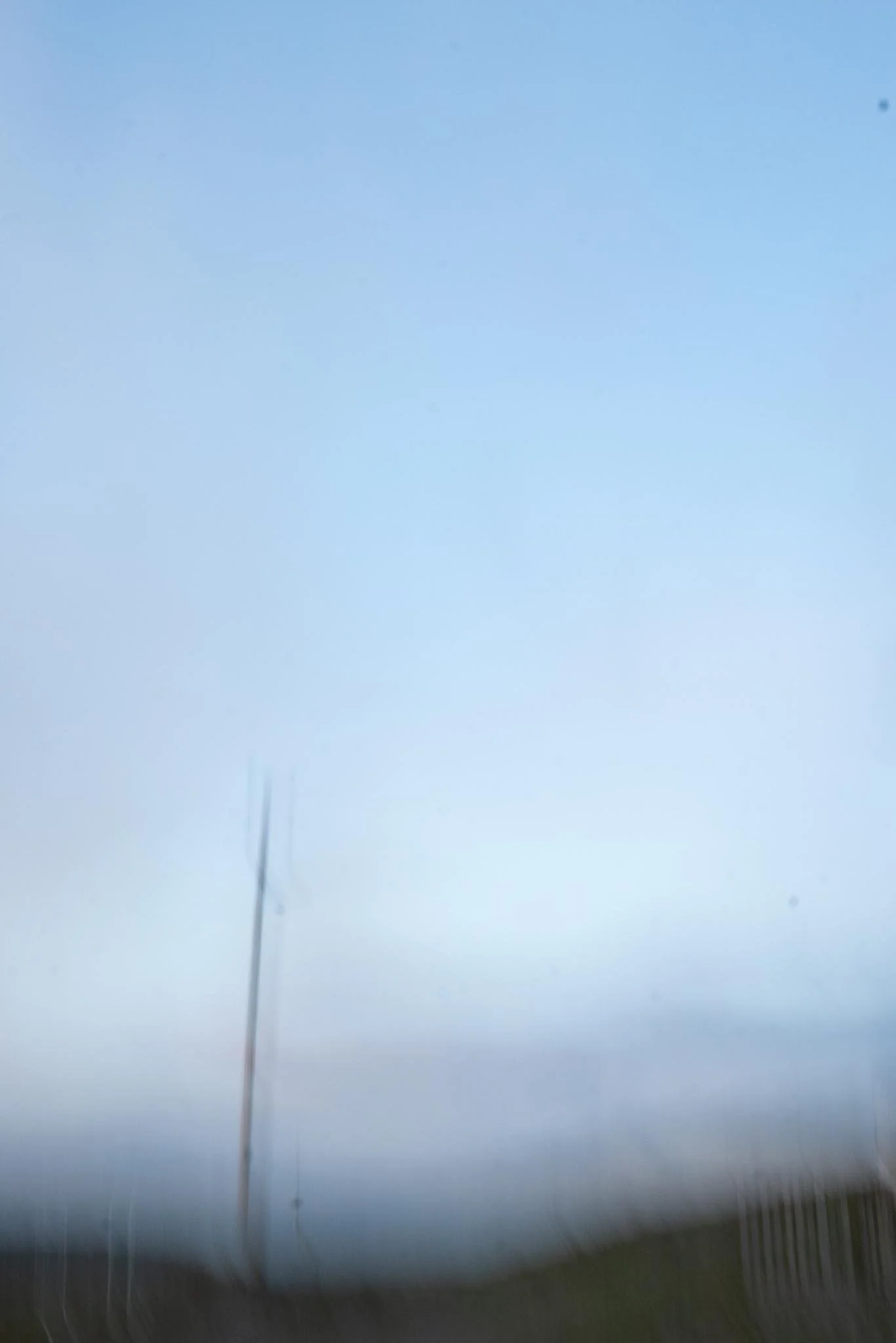 A blurred image of a road with a blue sky, faint streetlights, and a large, tall utility pole with a wire. West Cork. Abstract art