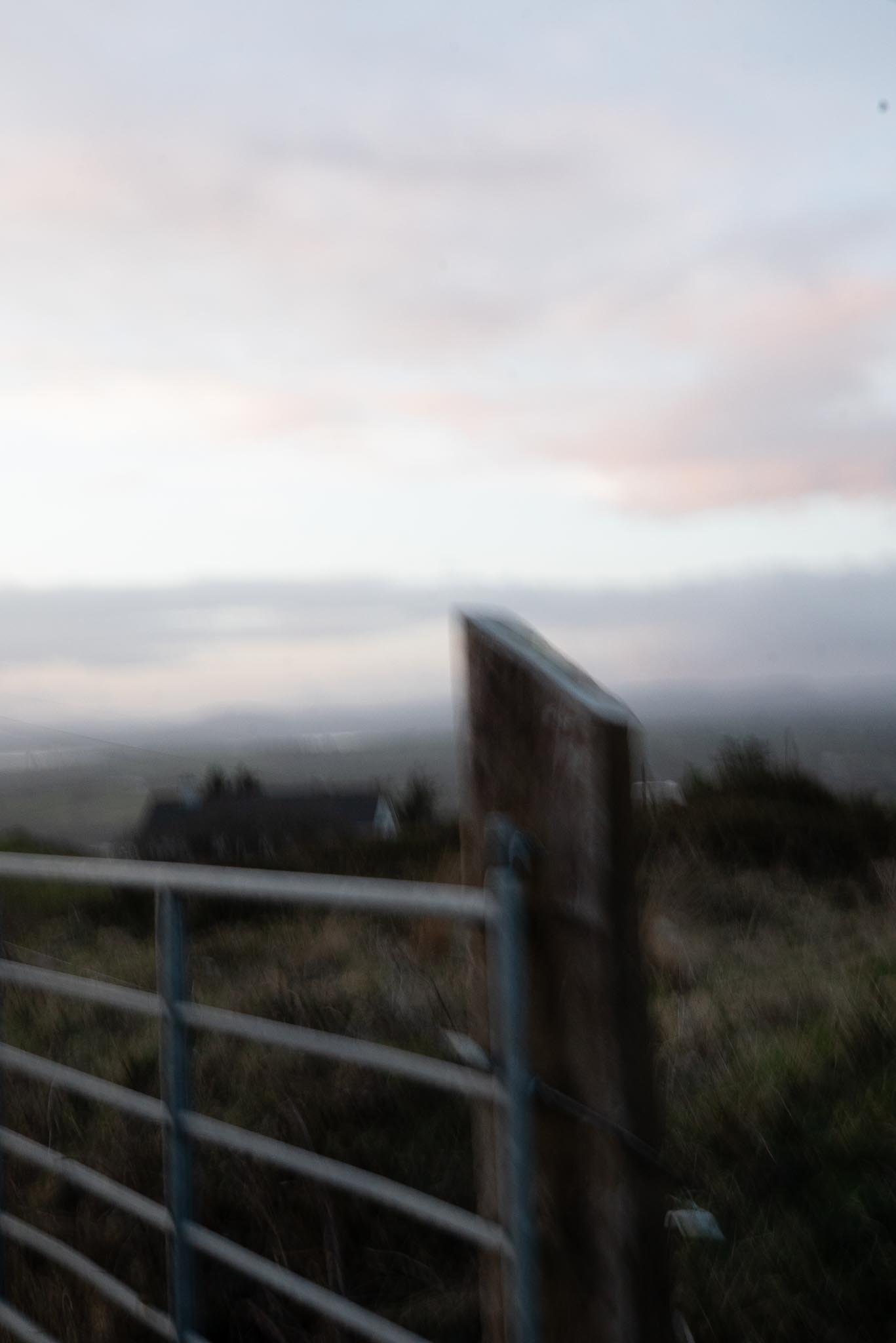 Blurry image of a wooden fence and a horizon with a cloudy sky at dusk or dawn. West Cork