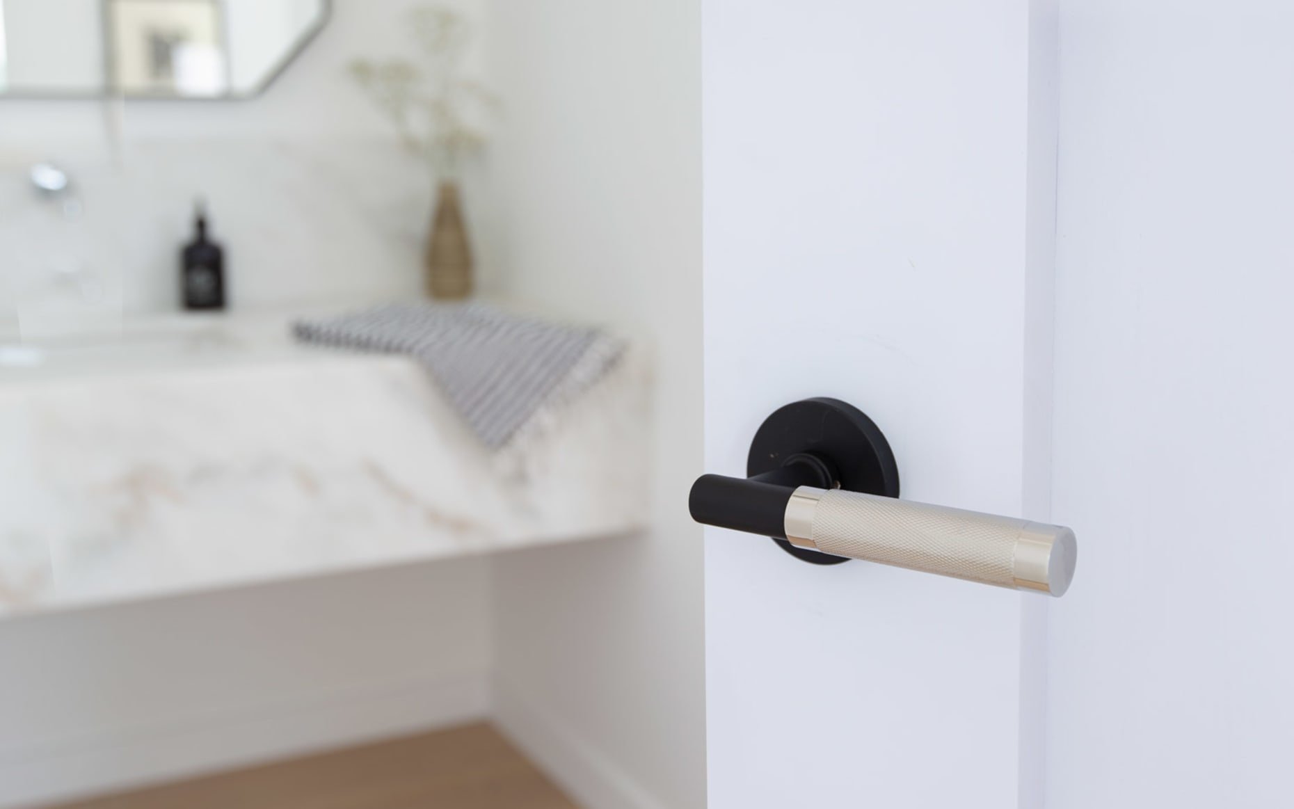 Close-up of a black and gold door handle on a white door in a bathroom or bedroom.