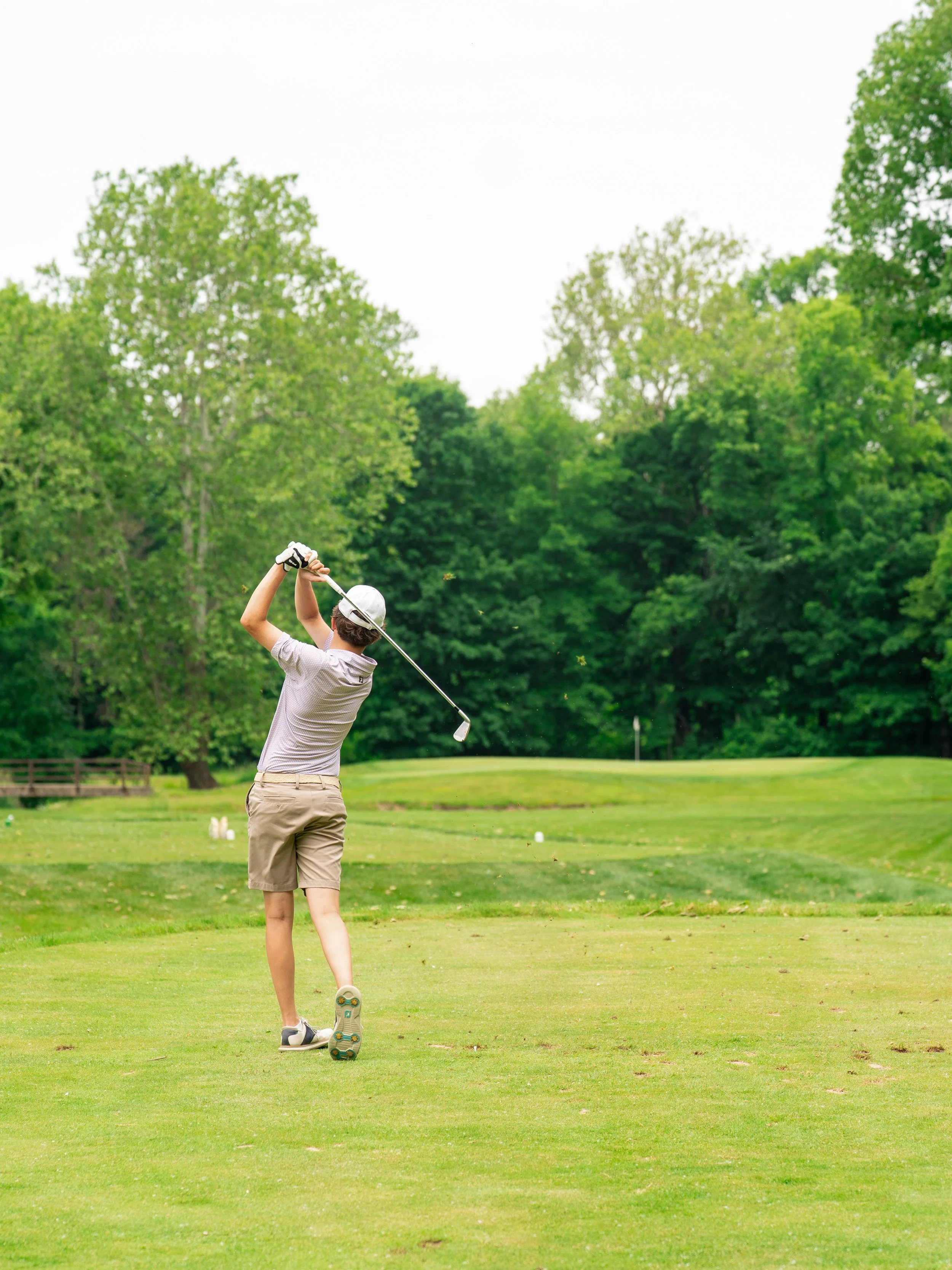 A person golf swinging on a lush green golf course surrounded by trees.
