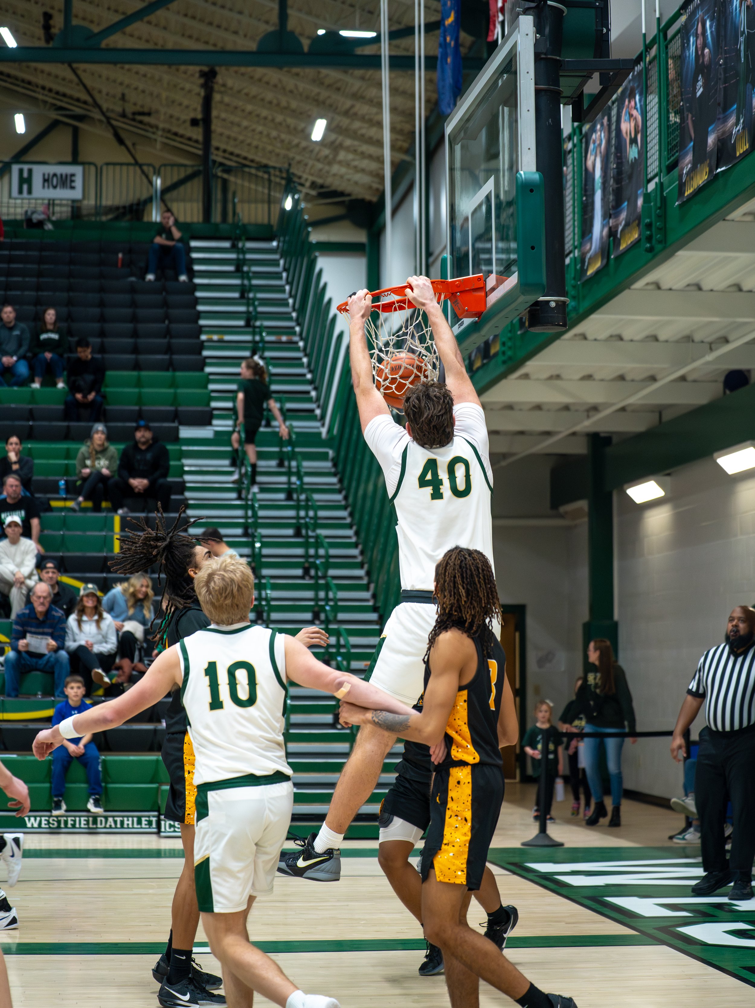 A basketball player wearing jersey number 40 is dunking the ball into the hoop, with other players nearby and spectators watching in the gymnasium.