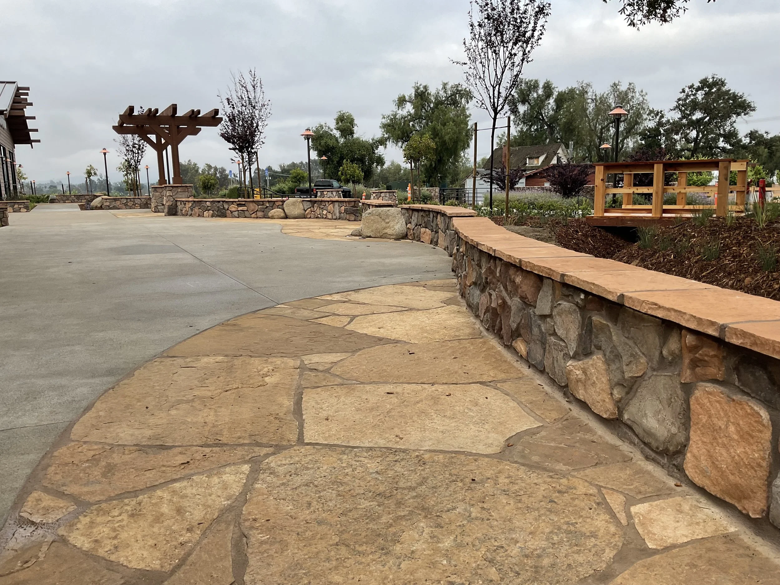 Curved sidewalk with stone border and landscaped garden areas, trees, and outdoor lighting.