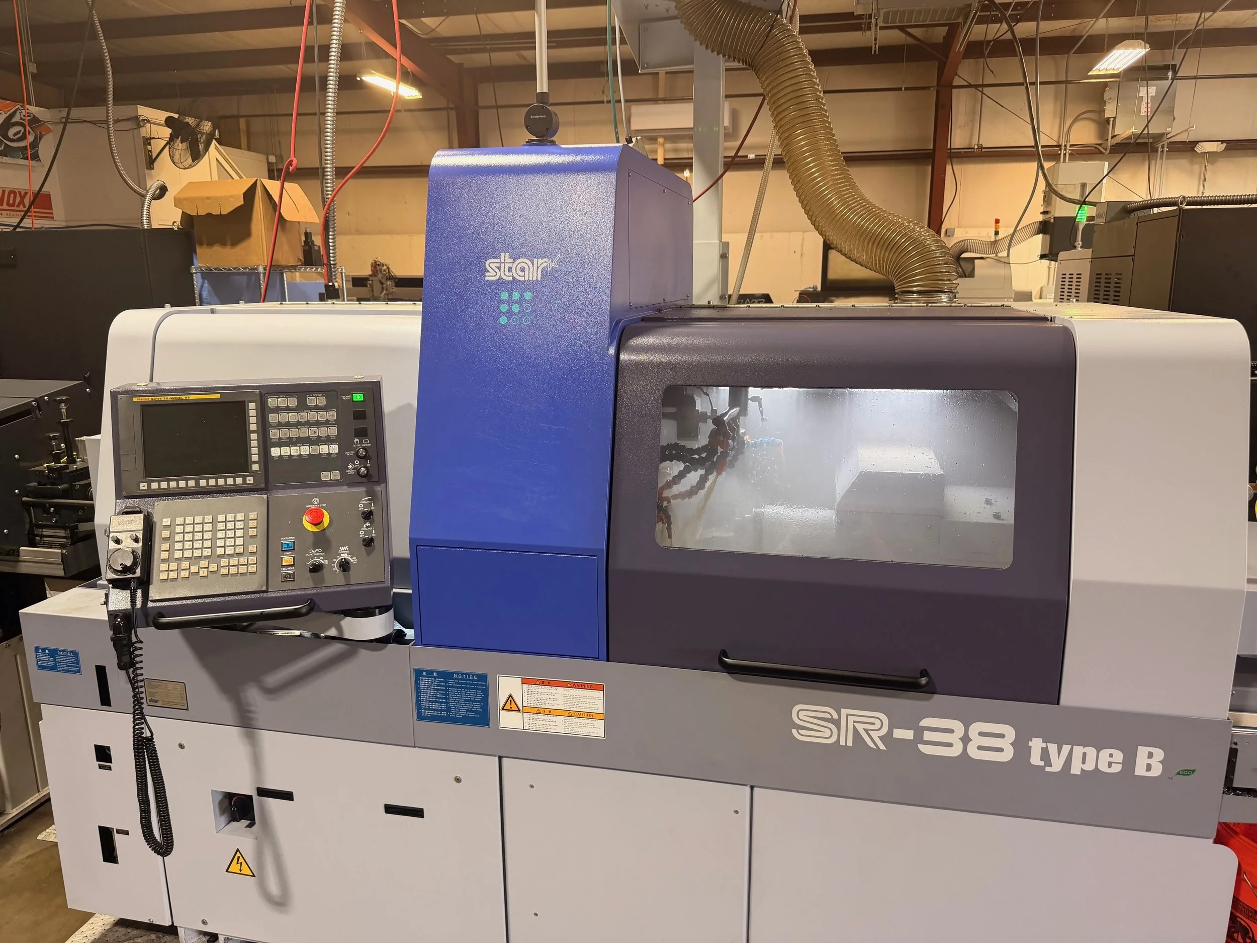 Industrial CNC machine labeled SR-38 type B, with control panel, in a factory setting with ducts and other equipment visible.