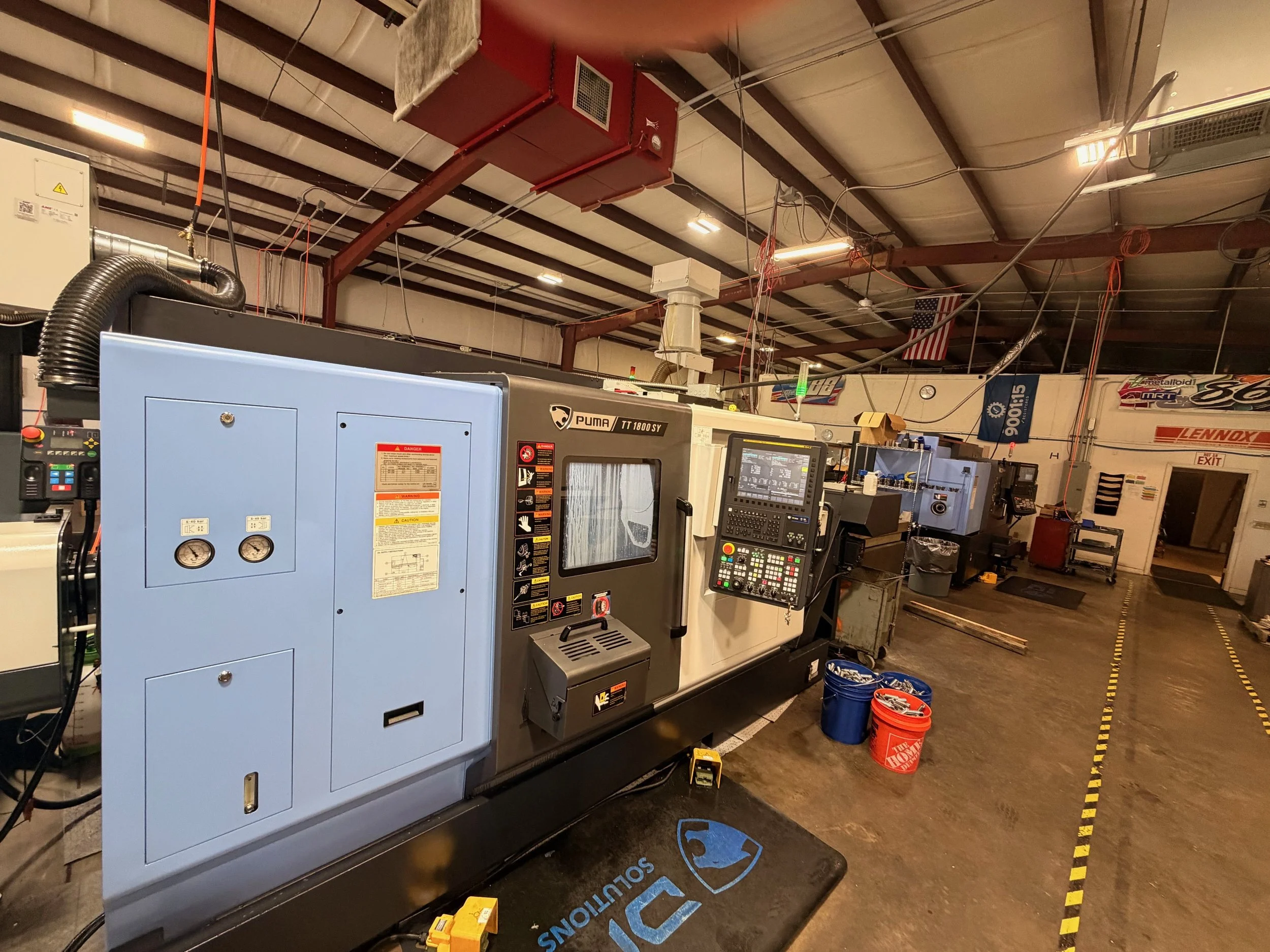 Industrial machine in manufacturing workshop with control panel, buckets, and safety markings on the floor.