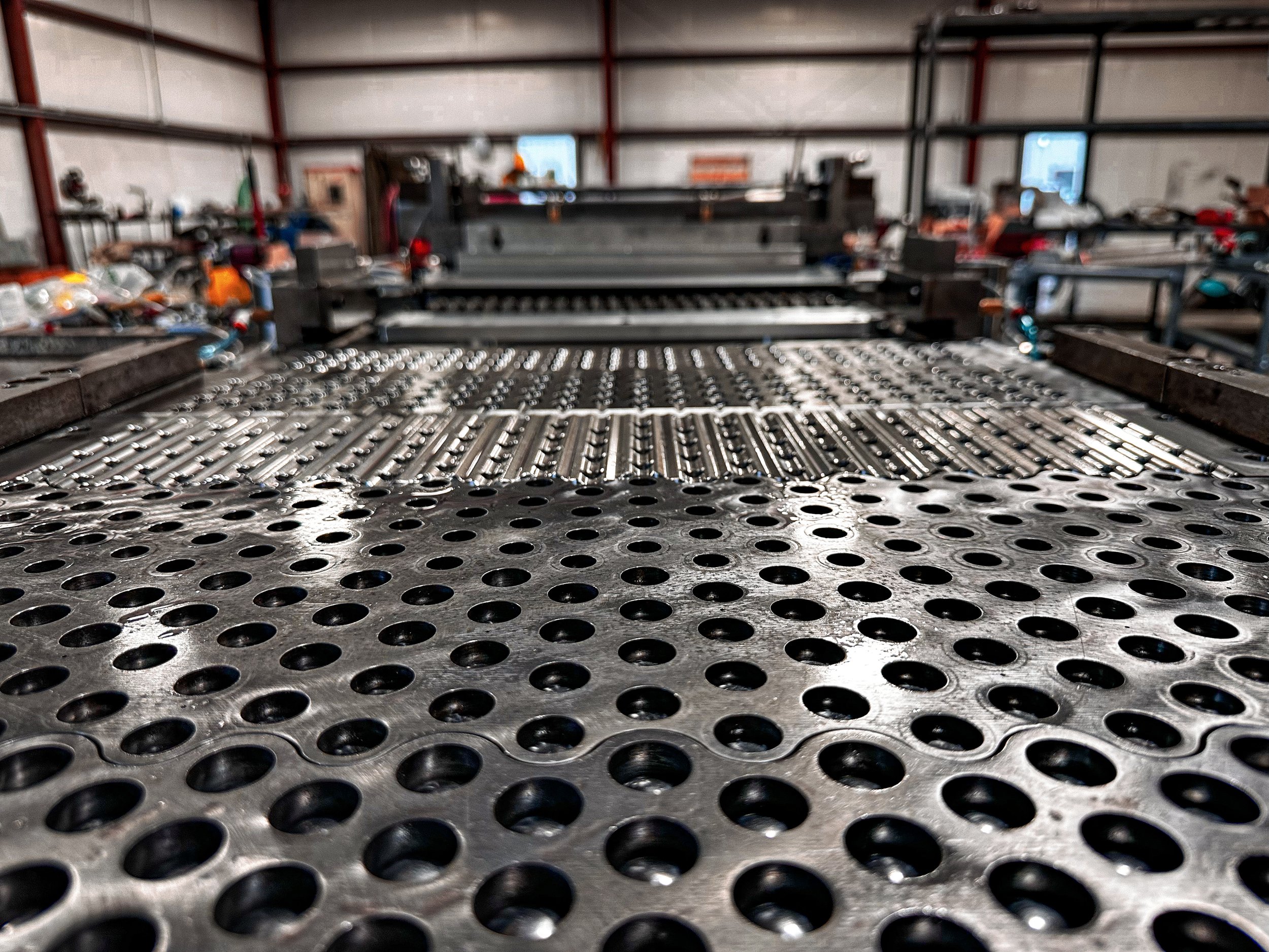 Close-up of a metal CNC machine bed with evenly spaced holes and linear rails in an industrial workshop.