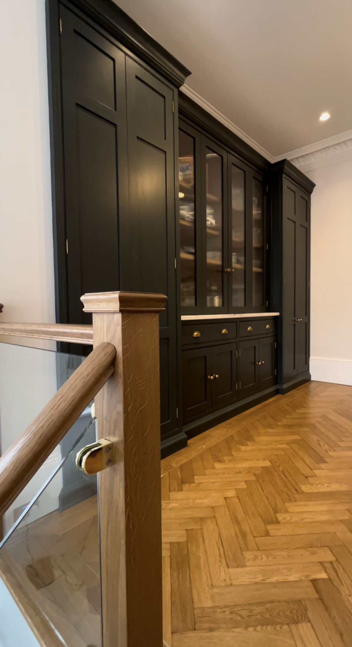 A black built-in cabinet with glass doors and brass knobs in a room with hardwood floor and white walls.