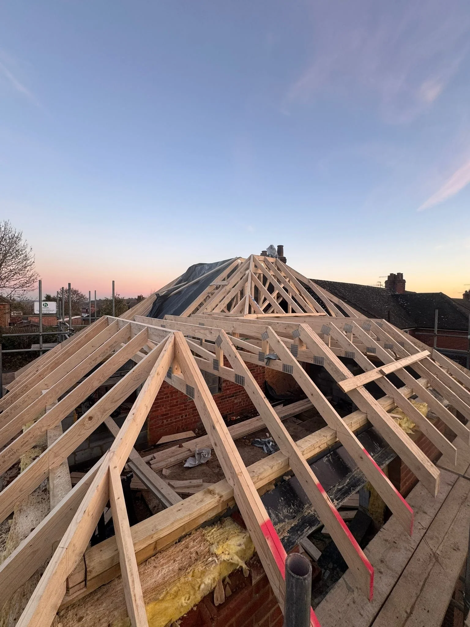 Construction site on a rooftop with wooden roof framing in progress at sunset.