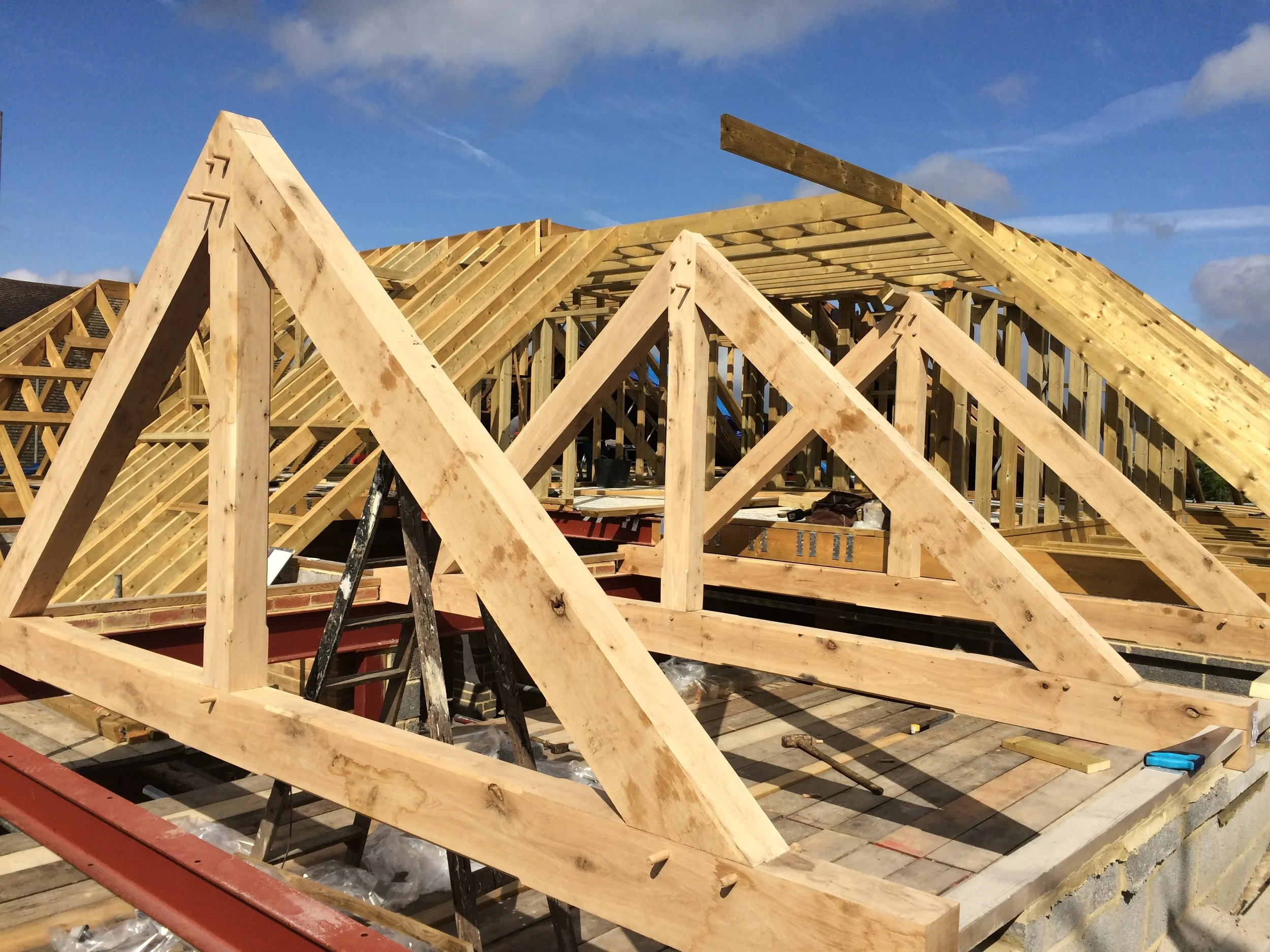 Construction site with wooden roof framing in progress, blue sky with some clouds.