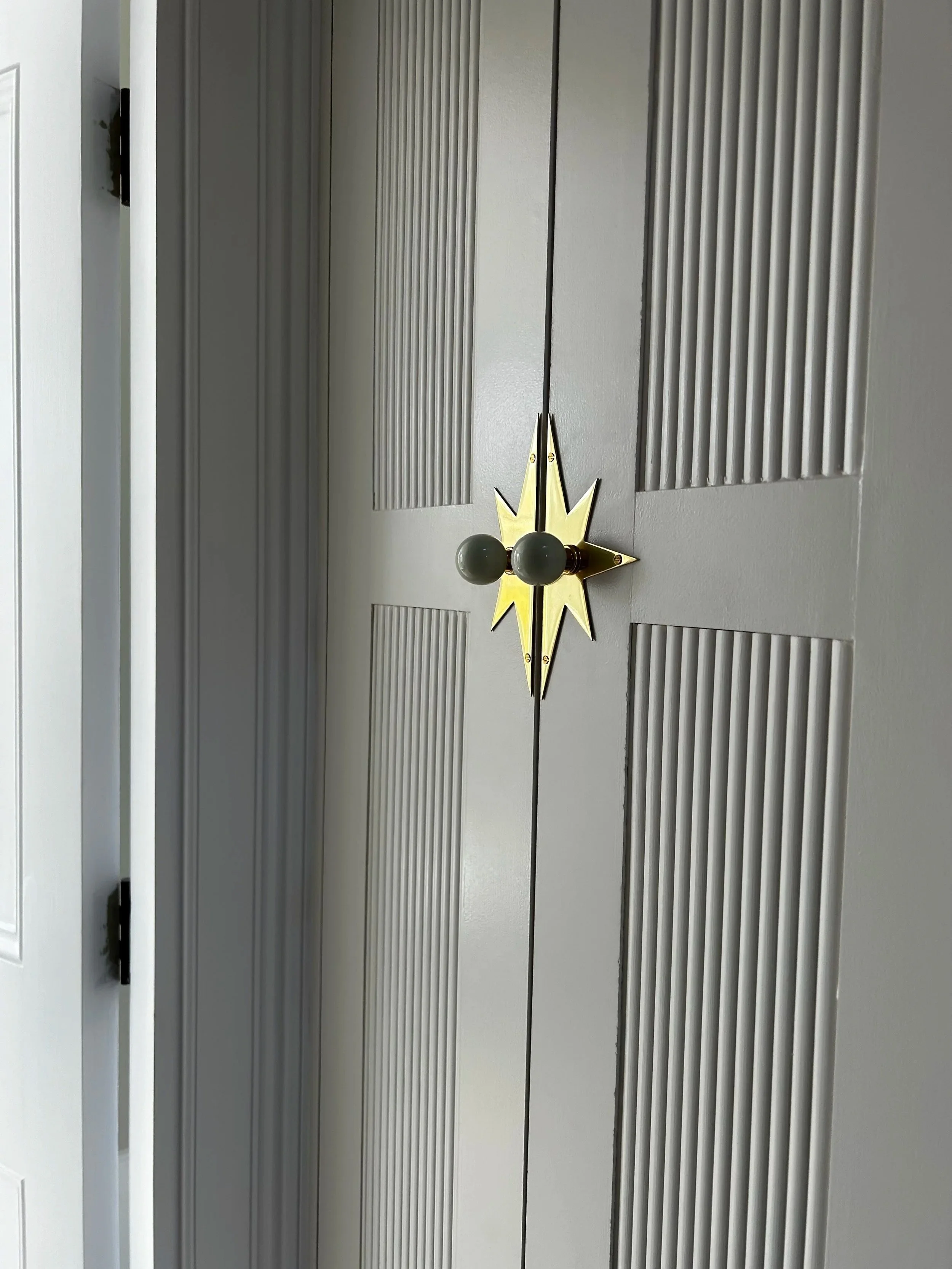 Decorative wall fixture with a starburst design and three dark spherical bulbs, mounted on a gray paneled wall.