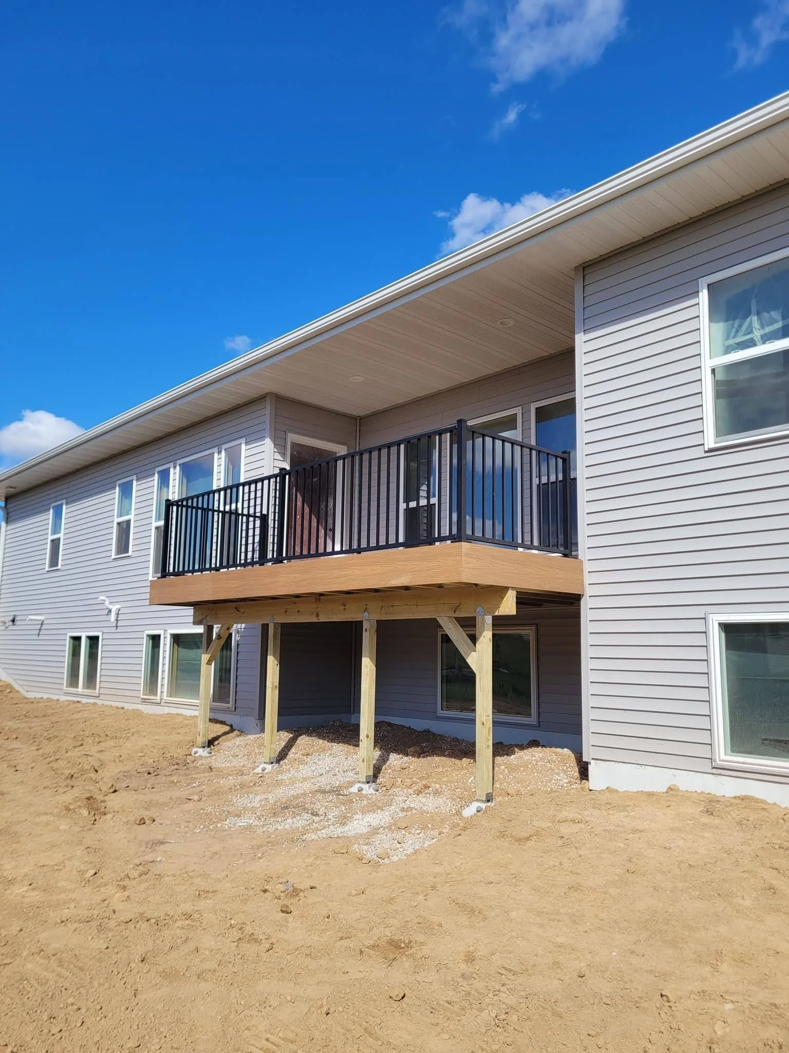 Newly built house with a second-floor balcony supported by wooden posts, with black metal railing, on a clear day with blue sky.