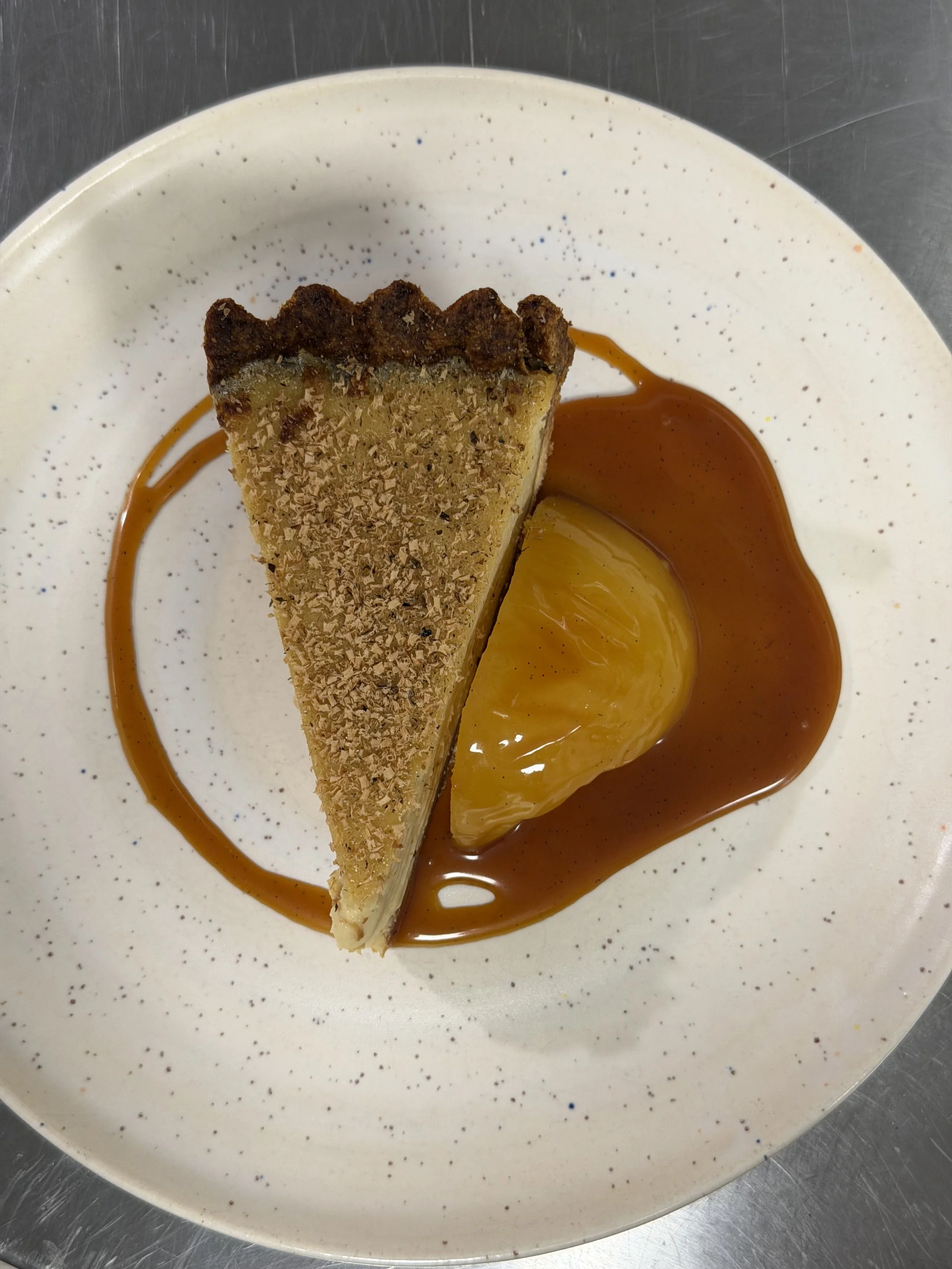 A slice of pie on a white plate with a caramel sauce and a lemon slice garnished on top.