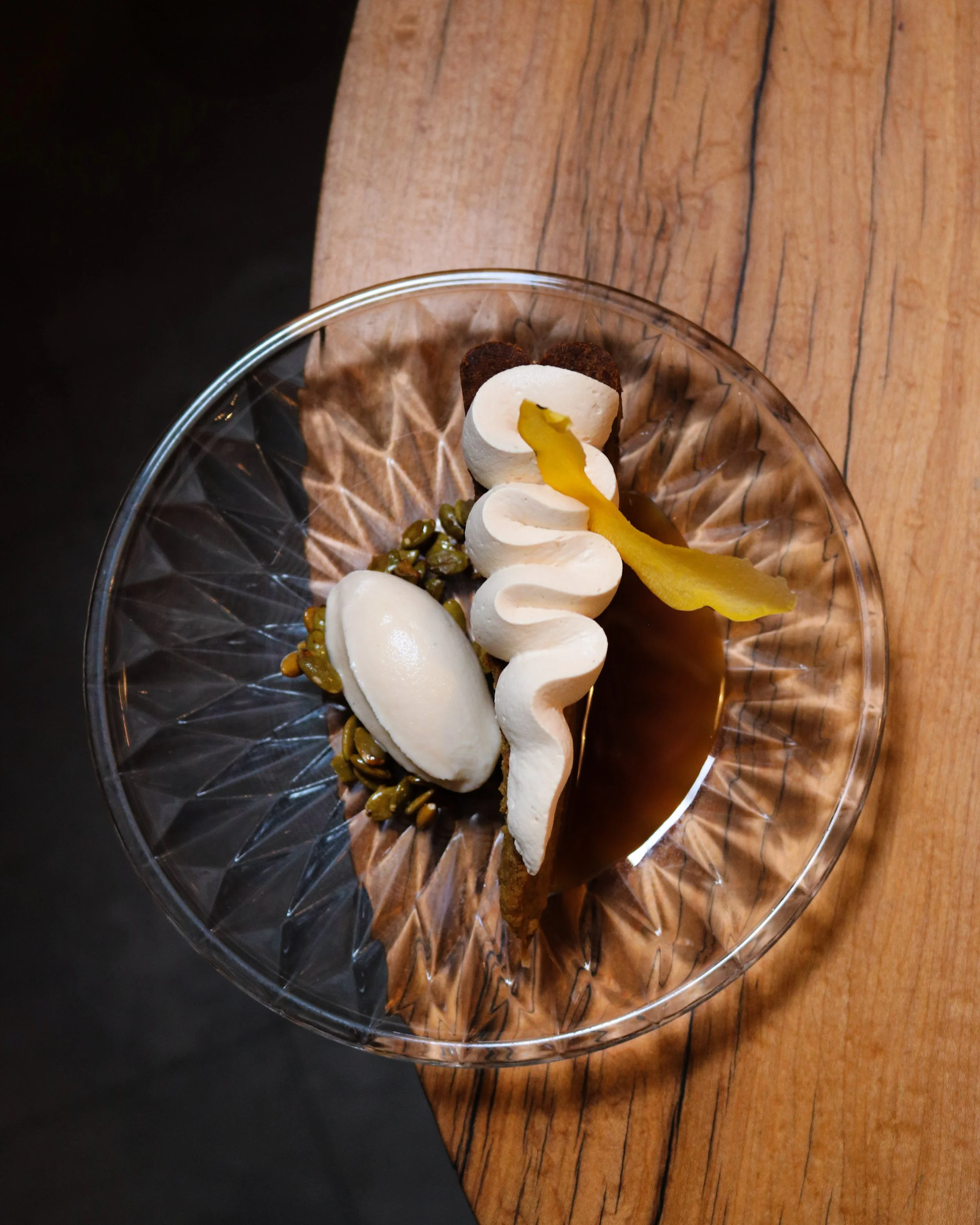 Dessert served in a glass dish with whipped cream, caramel sauce, a cookie, a scoop of ice cream, a yellow garnish, and seeds.