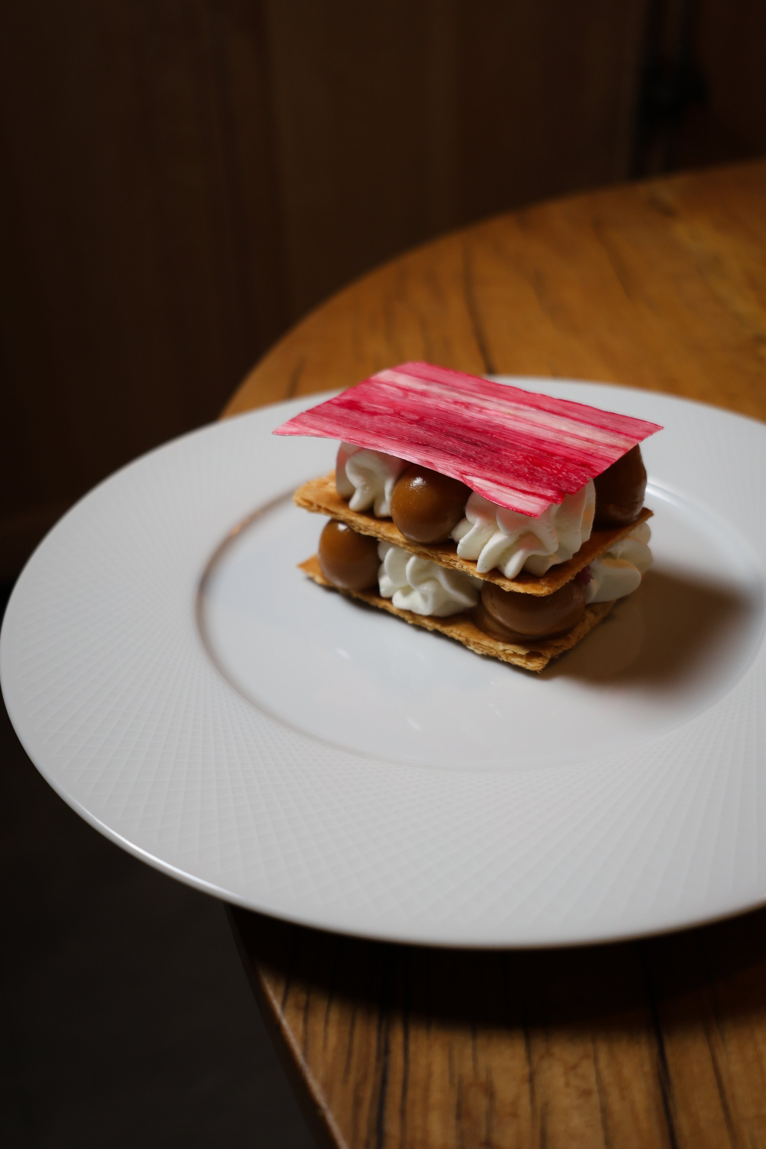 Dessert with layers of cream, chocolate, and a pink decorative top, served on a white plate.