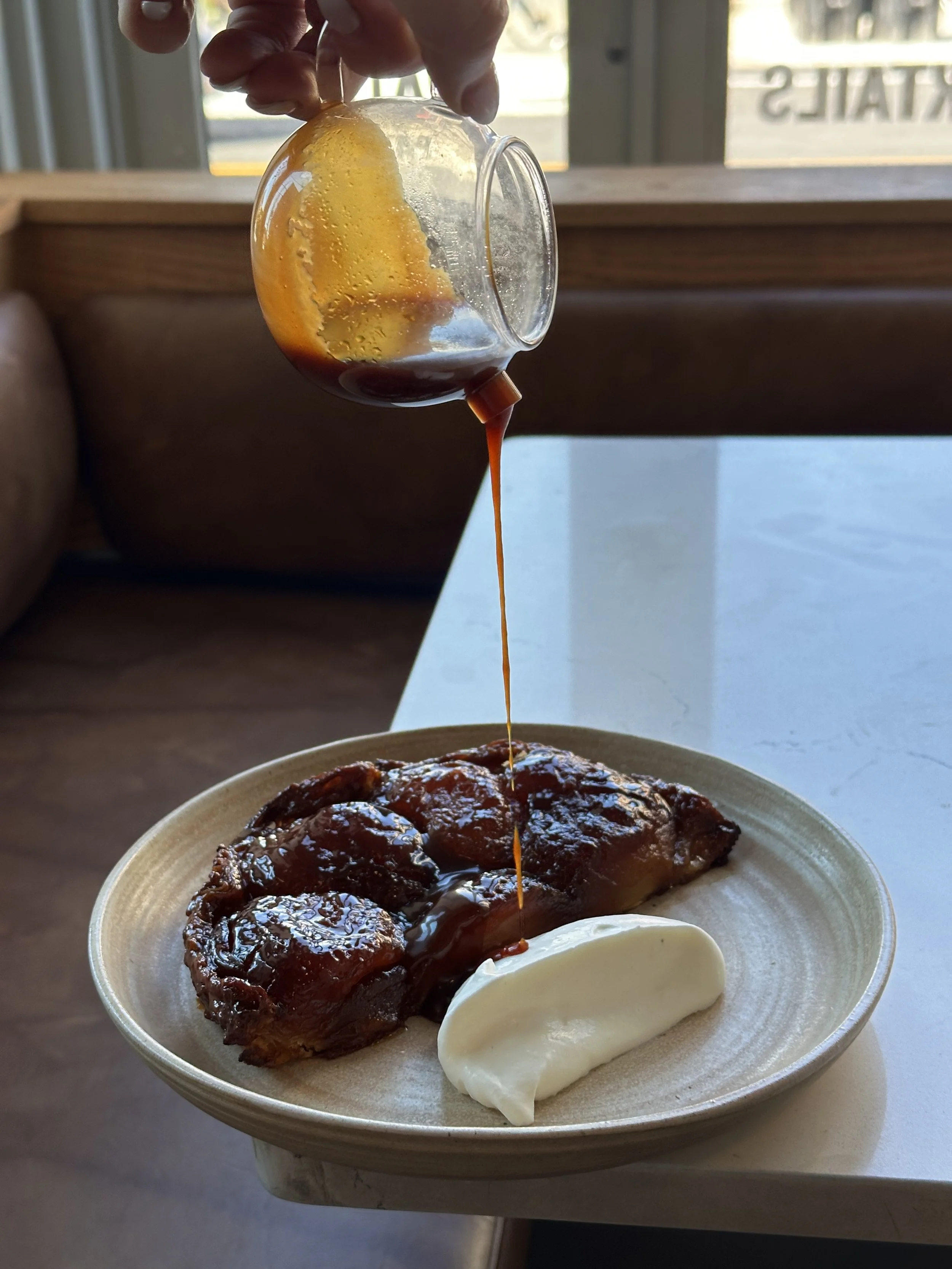 Barbecue chicken with sauce on a plate with a dollop of mayonnaise, and dark liquid sauce being poured from a glass container.