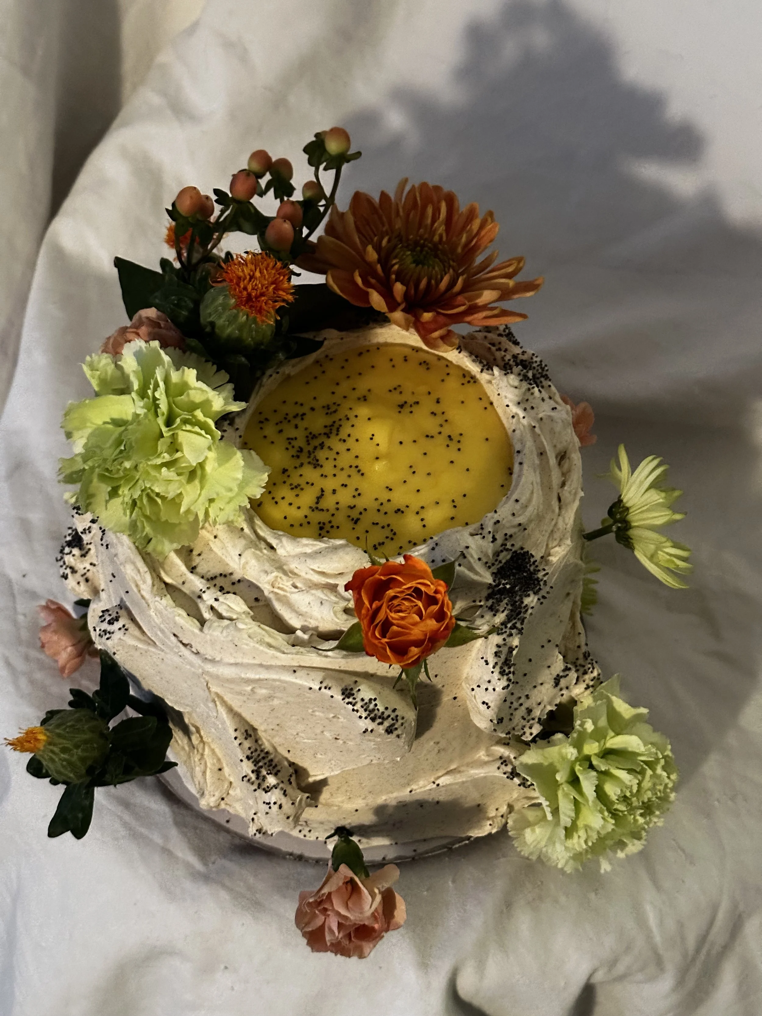 Cake decorated with fresh flowers and a yellow filling, topped with black sprinkles.