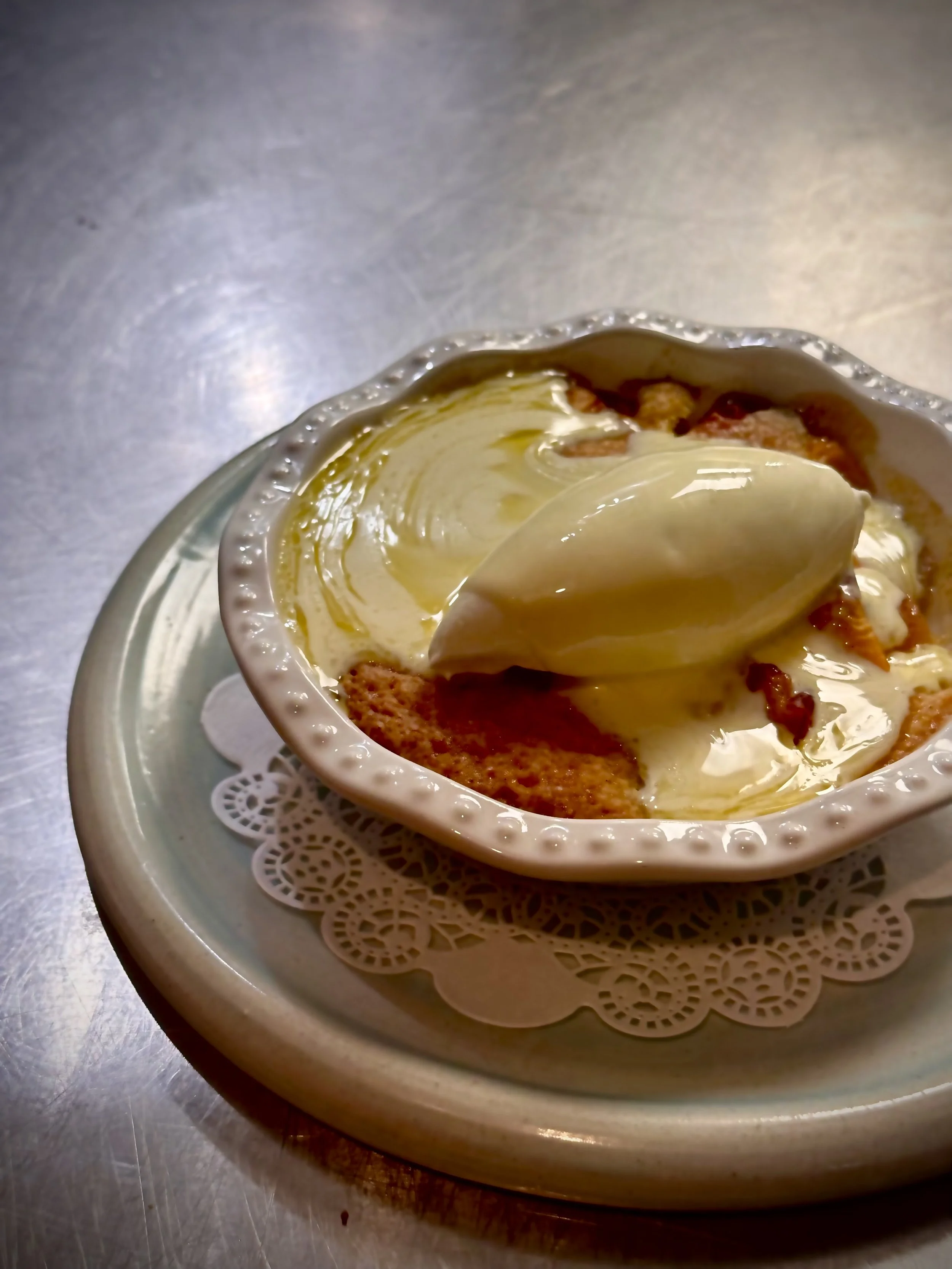 A bowl of dessert with vanilla ice cream and caramel sauce on top, served on a decorative doily placed on a plate.