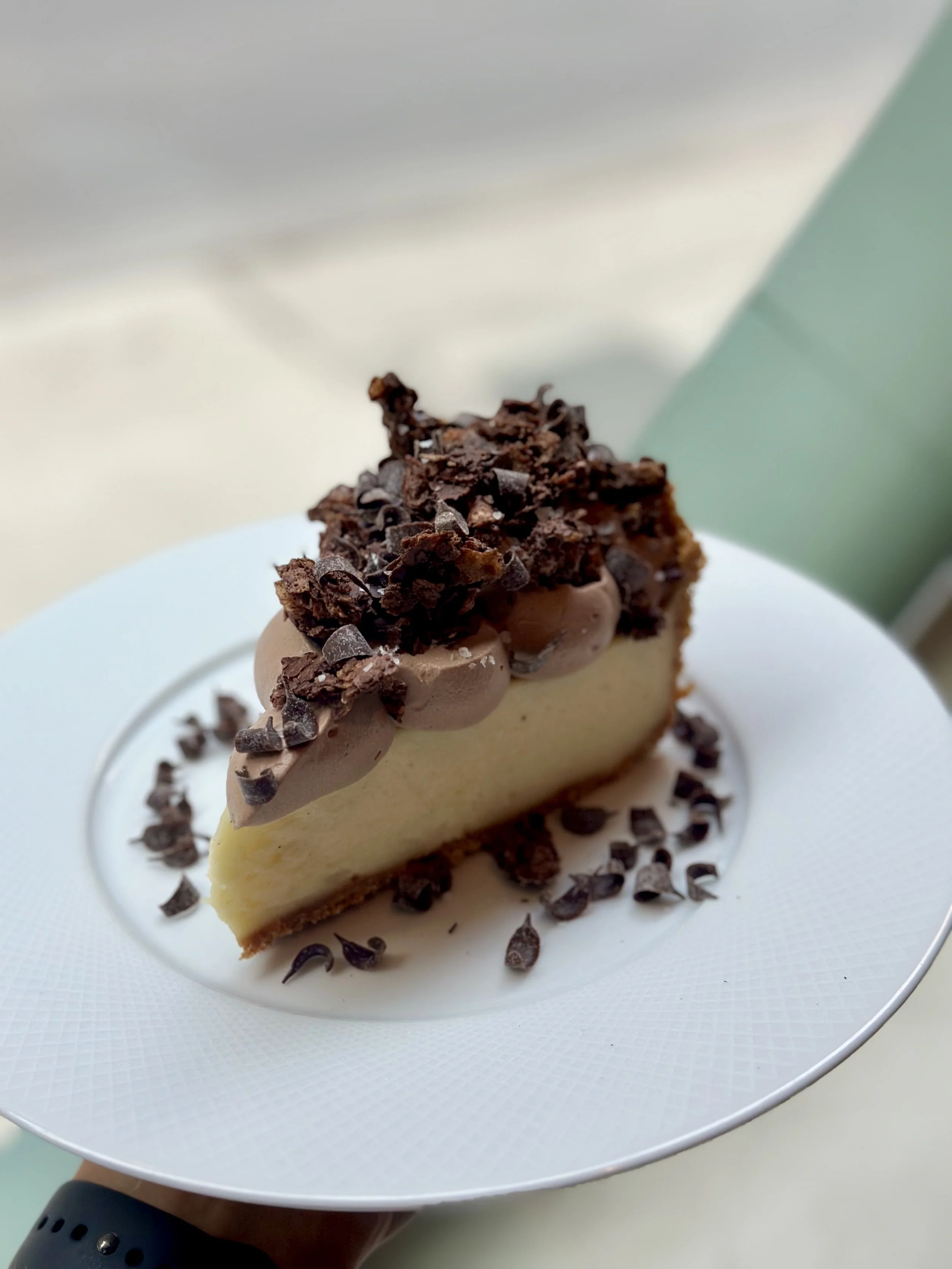 A slice of chocolate and vanilla cheesecake topped with chocolate shavings on a white plate.