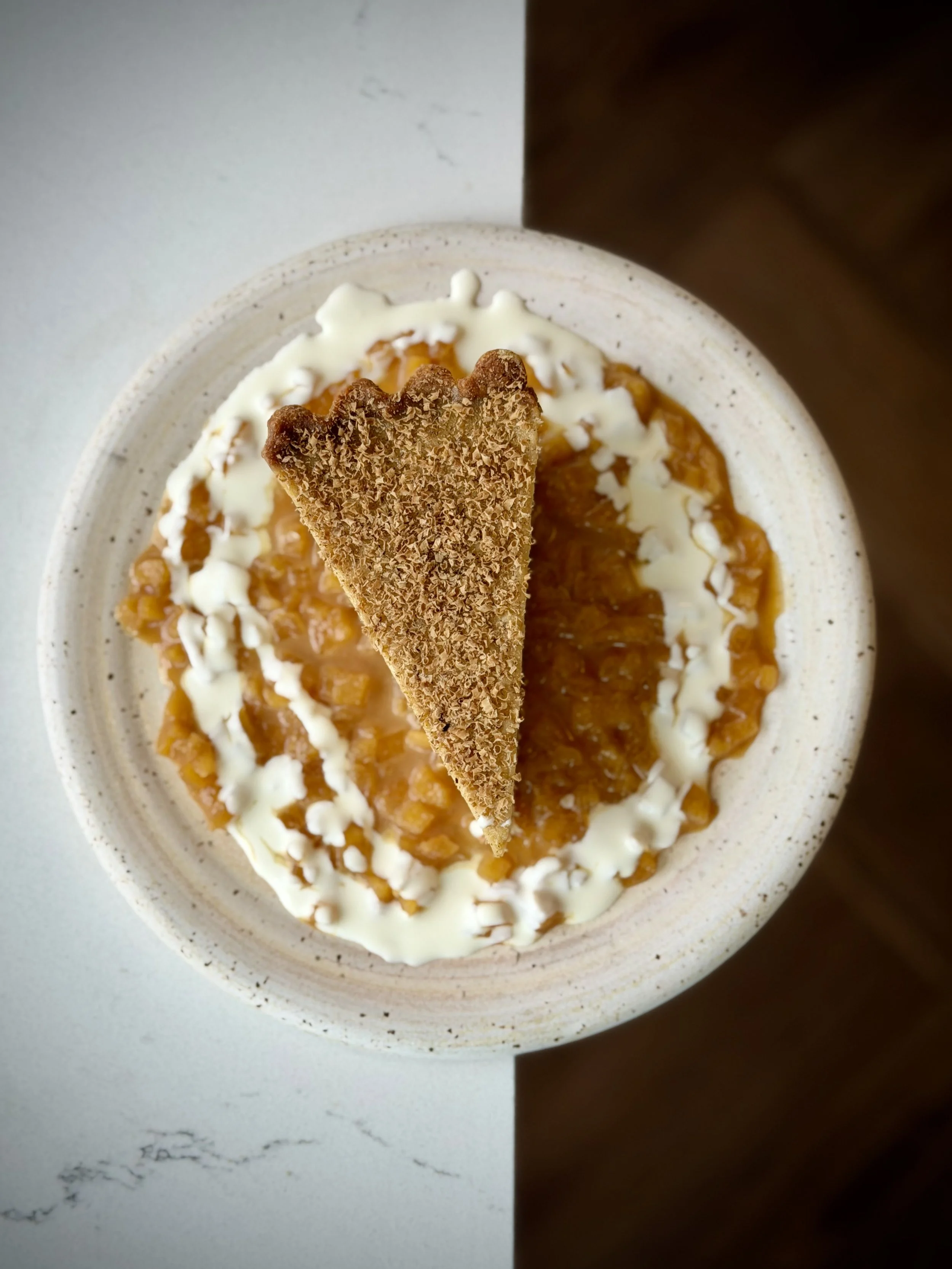 A bowl with apple crisp topped with a ring of white icing and a triangular piece of graham cracker crust on top.