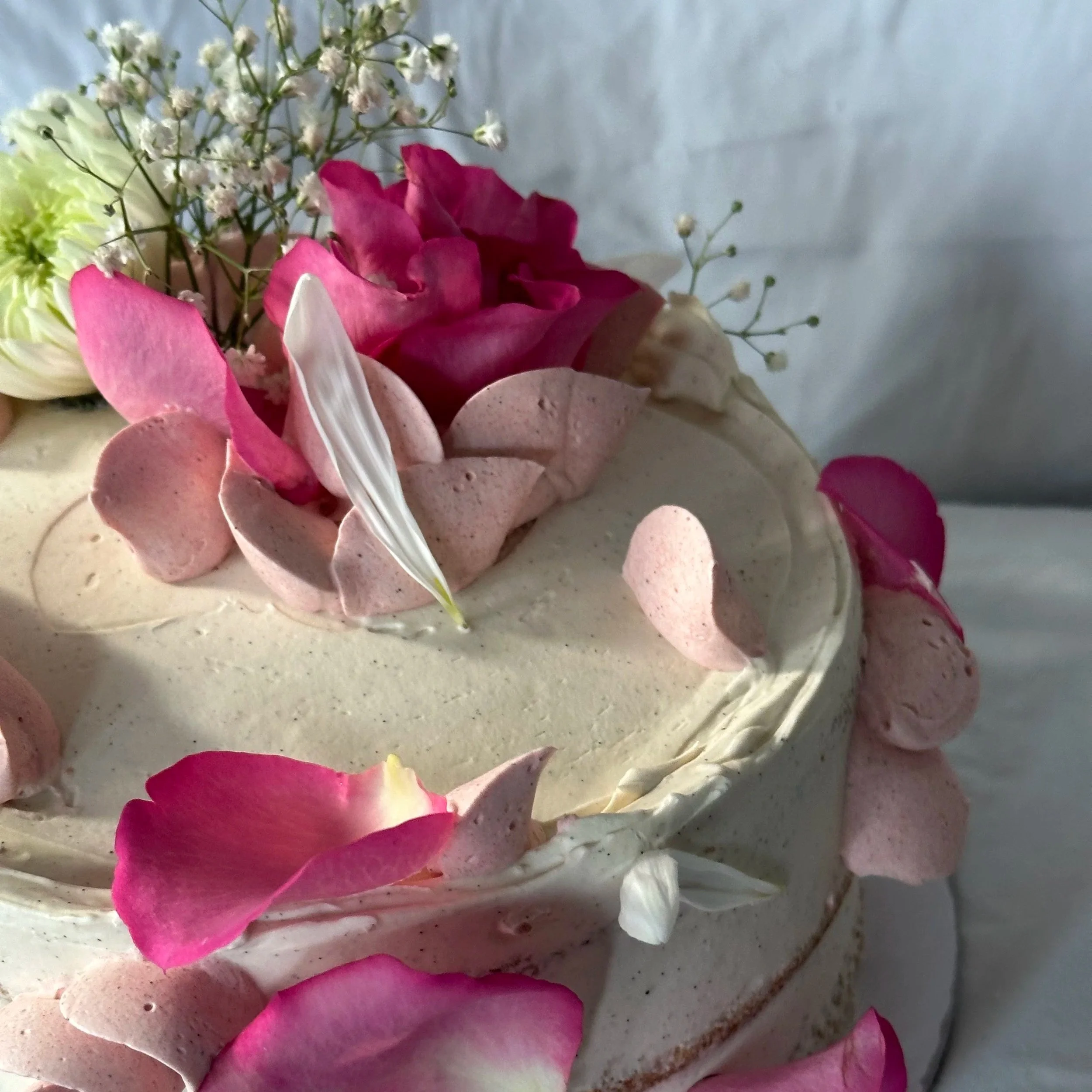 Close-up of a wedding cake decorated with pink and white flower petals and small white flowers.