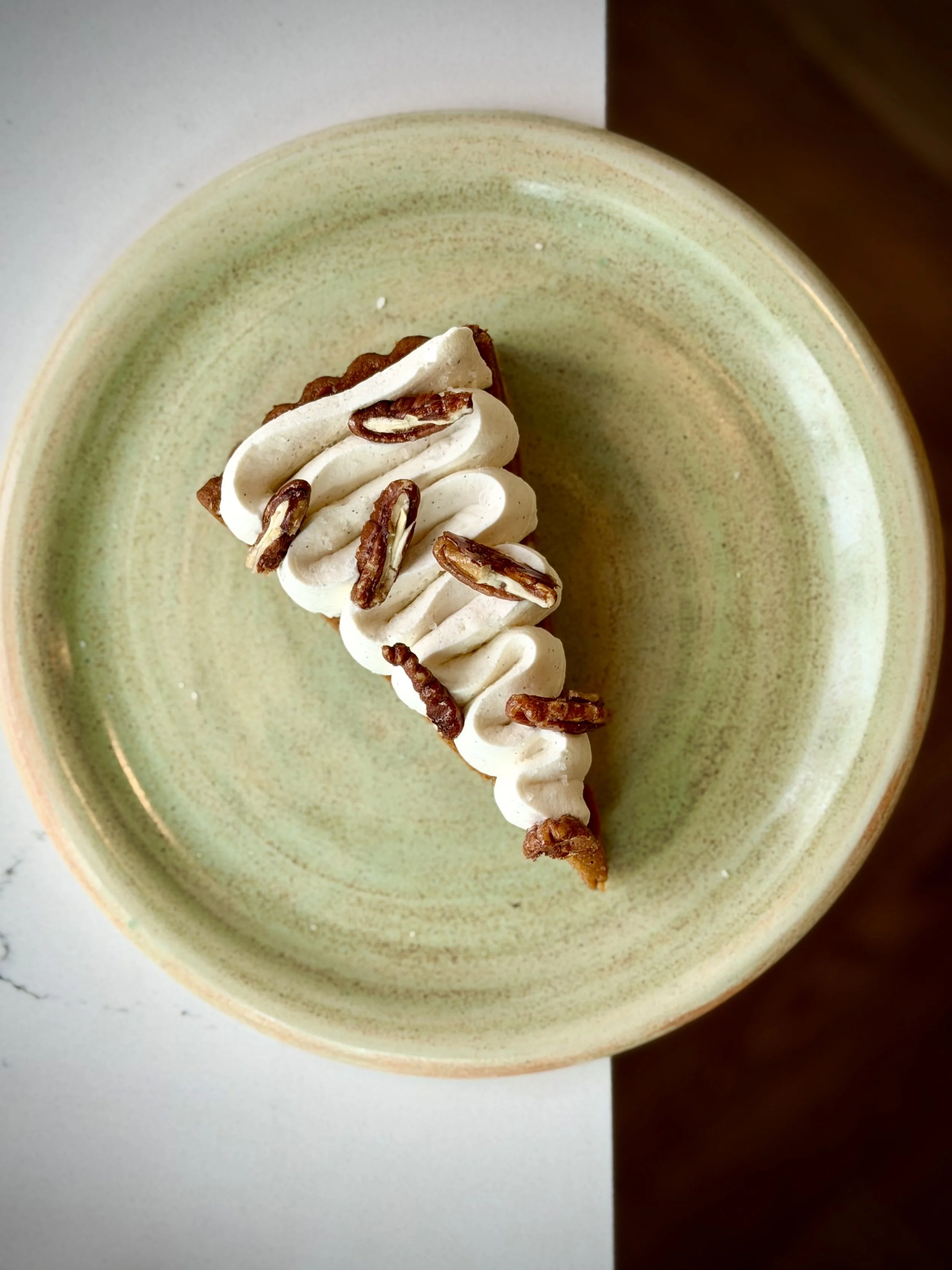 A piece of pie topped with whipped cream and pecans on a light green ceramic plate.