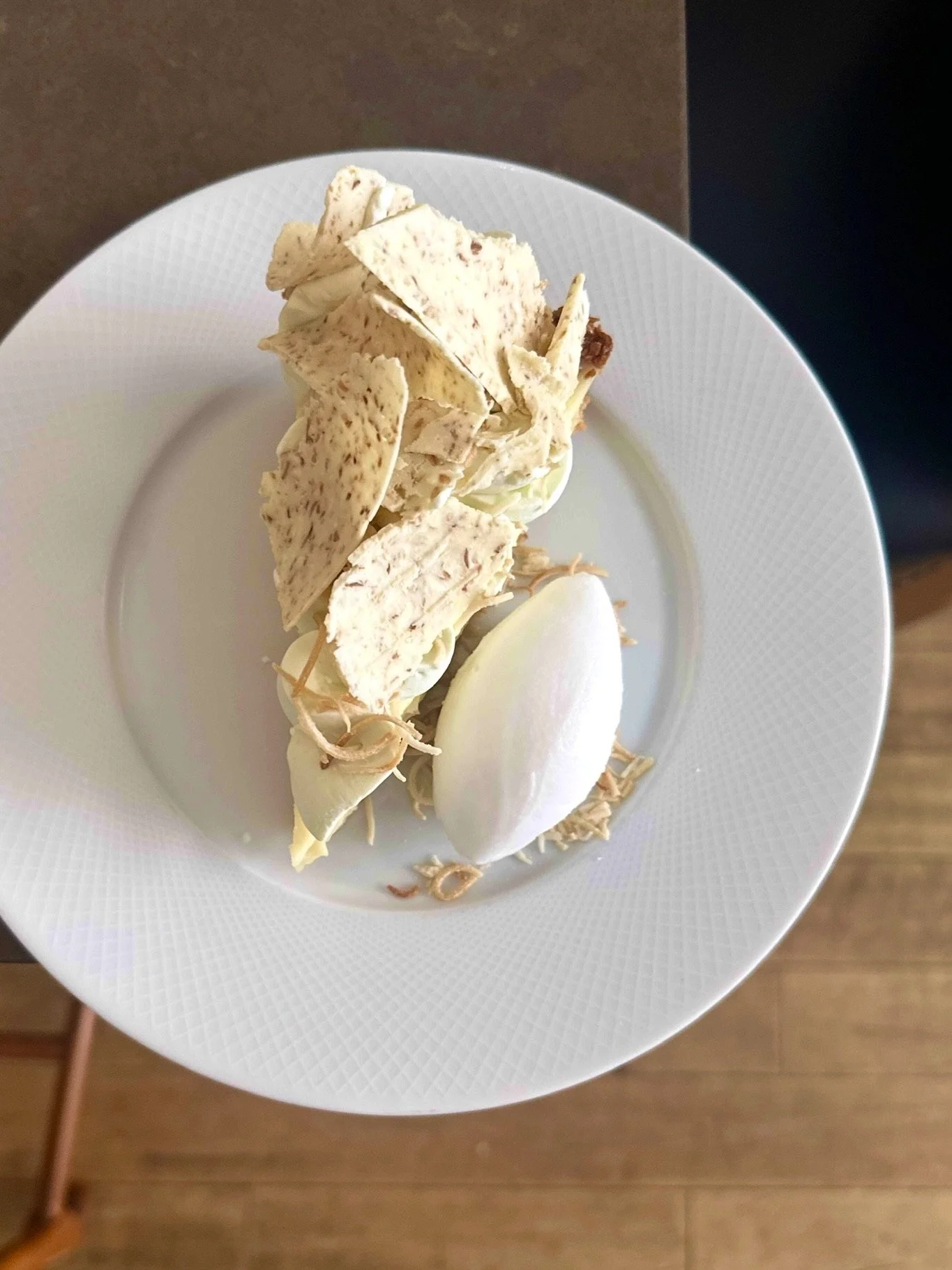 A plate with pieces of white chocolate and a scoop of vanilla ice cream.