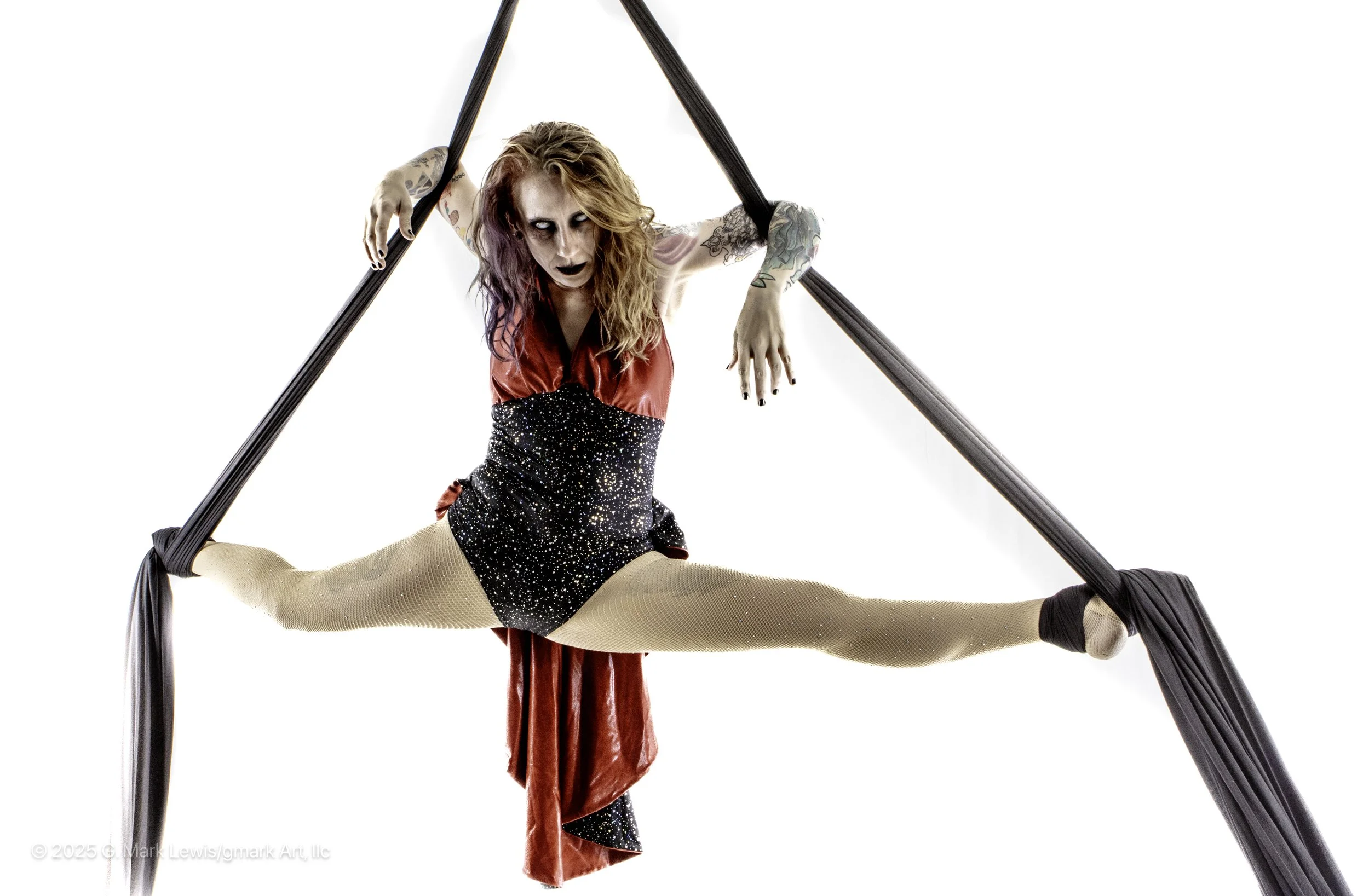 Zomibe Love is in a left sided front split on a black silks. She is wearing black and red costume.