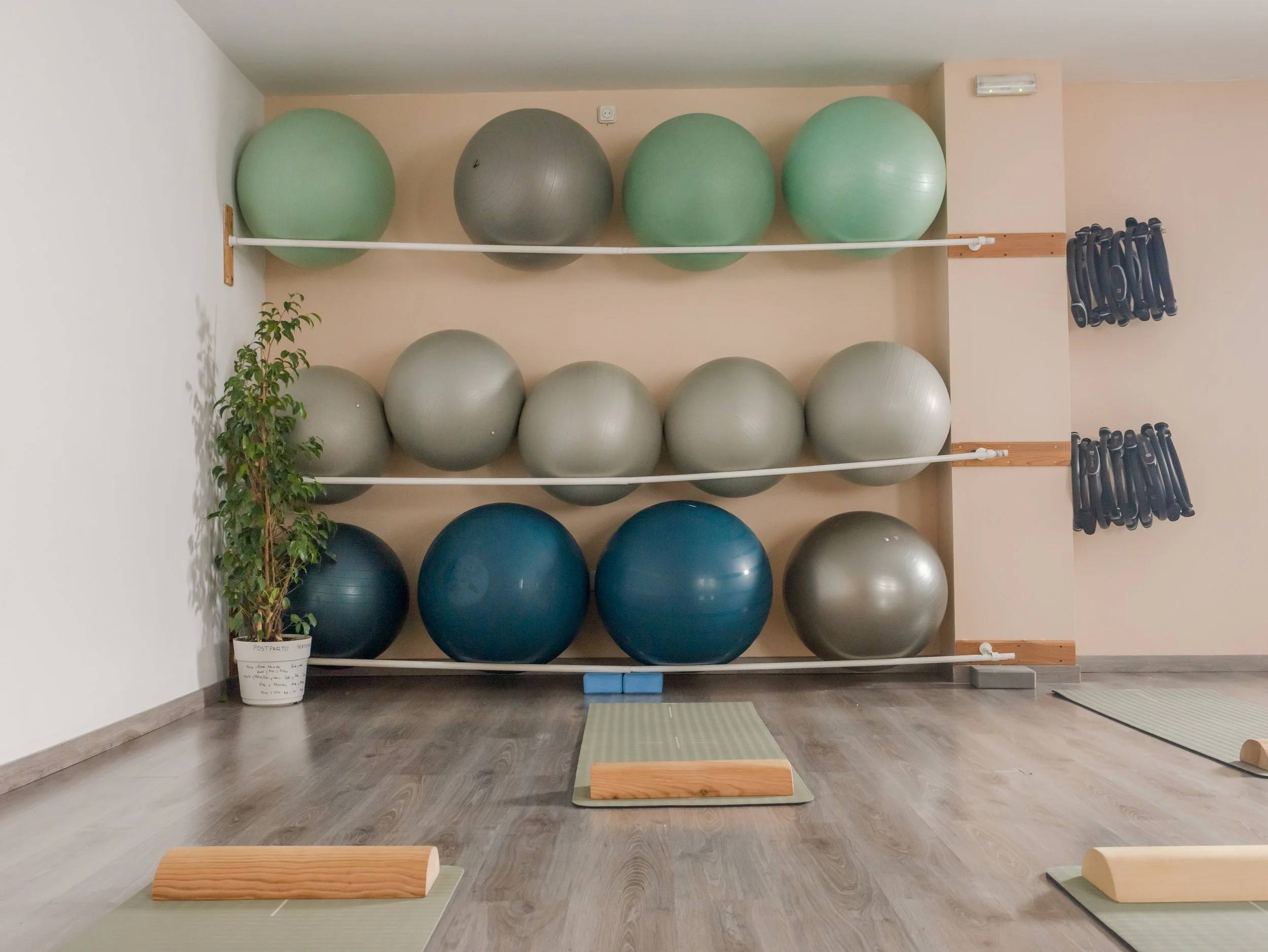 Sala de ejercicio con pelotas de estabilidad en estantes, tapetes de yoga, bloques y ruedas de espuma en un espacio de gimnasio o estudio de yoga.
