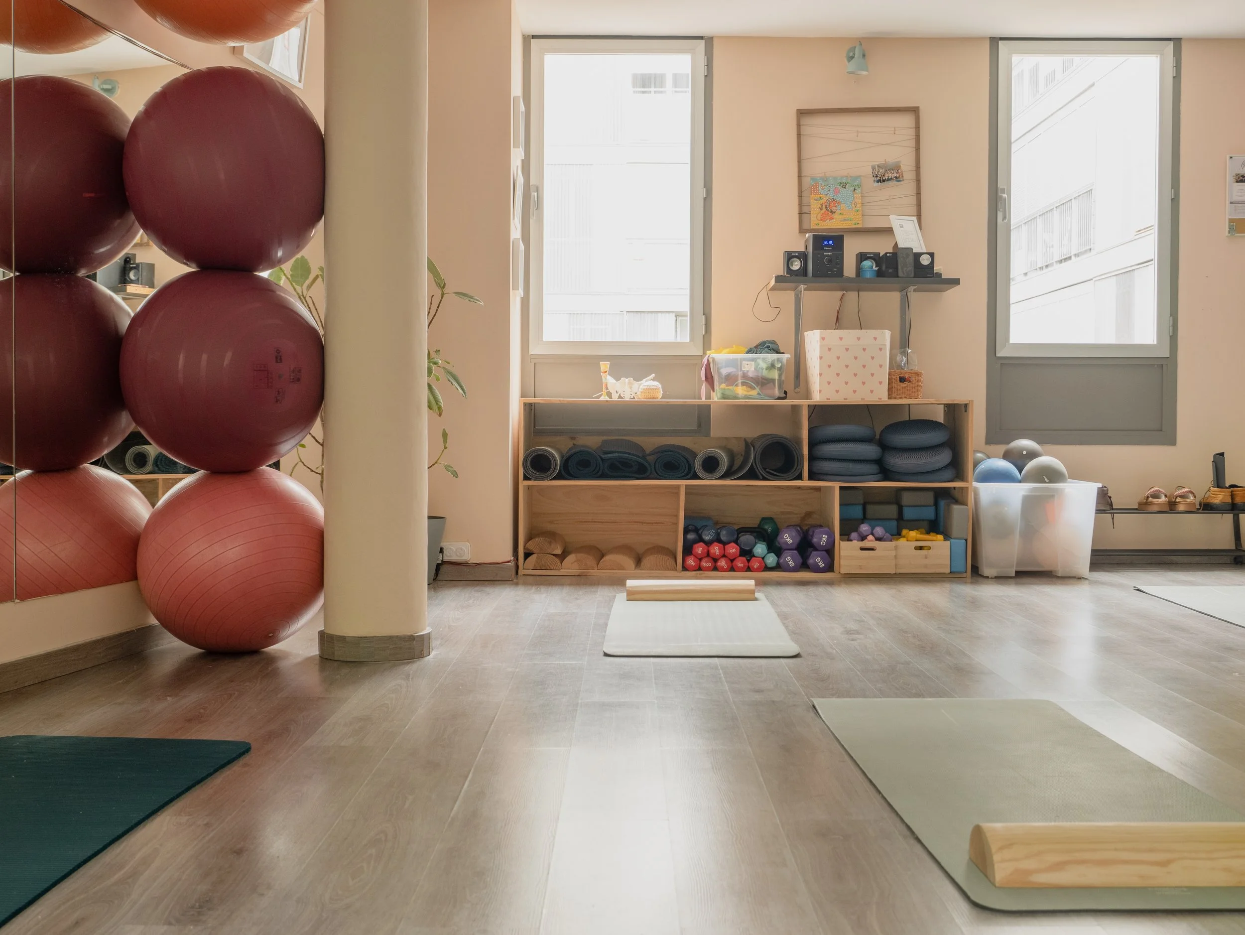 Sala de yoga con esterillas, pelotas de ejercicio, mancuernas y equipo de entrenamiento organizado en estantes digitales con ventanas pequeñas y luz natural