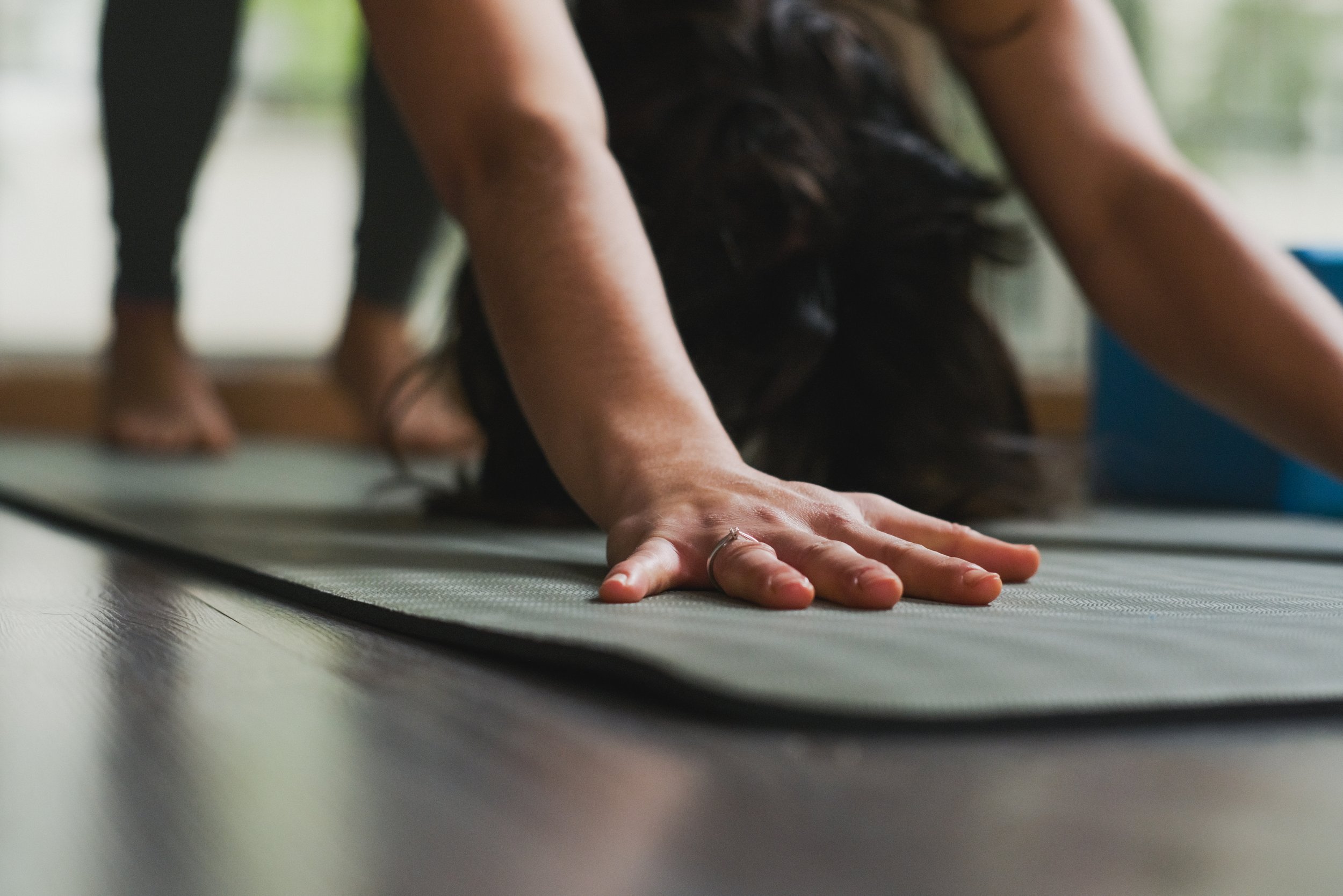 Persona en posición de yoga en un tapete de ejercicio, con manos extendidas hacia adelante y cabeza inclinada hacia el suelo, en un ambiente interior