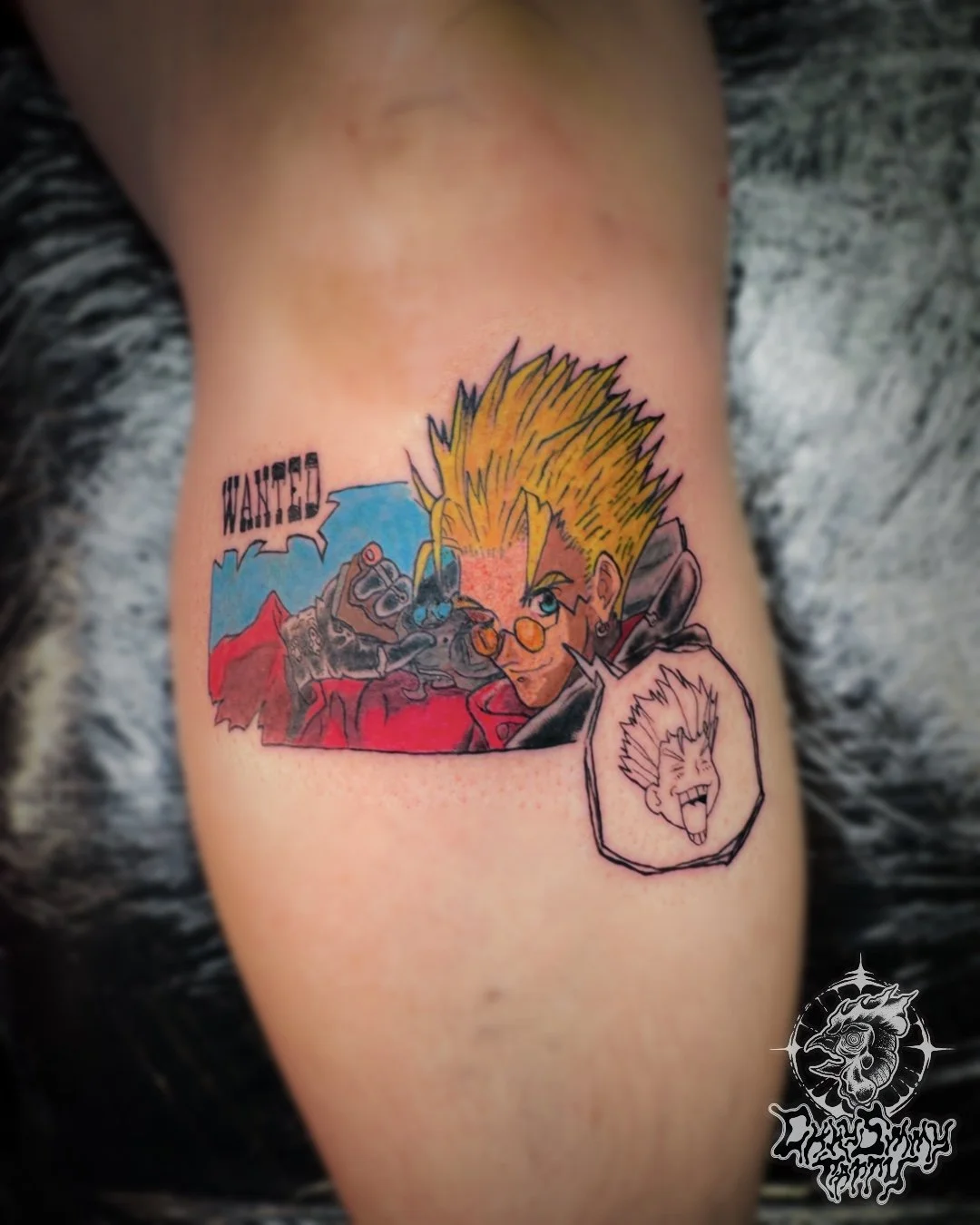 Colorful tattoo of Vash the stampede with spiky yellow hair and sunglasses, with the word 'WANTED!' above, and a small black-and-white cartoon face of a screaming person in an oval on the right side.
