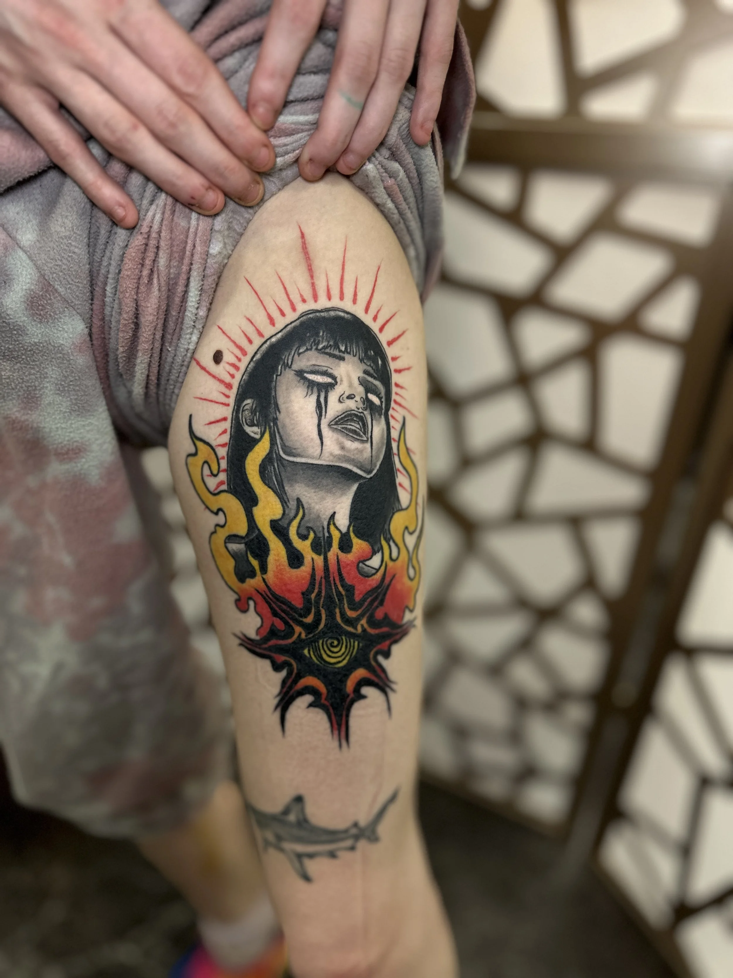 Tattoo of a woman with tears, flames, and a spiral eye on the arm.