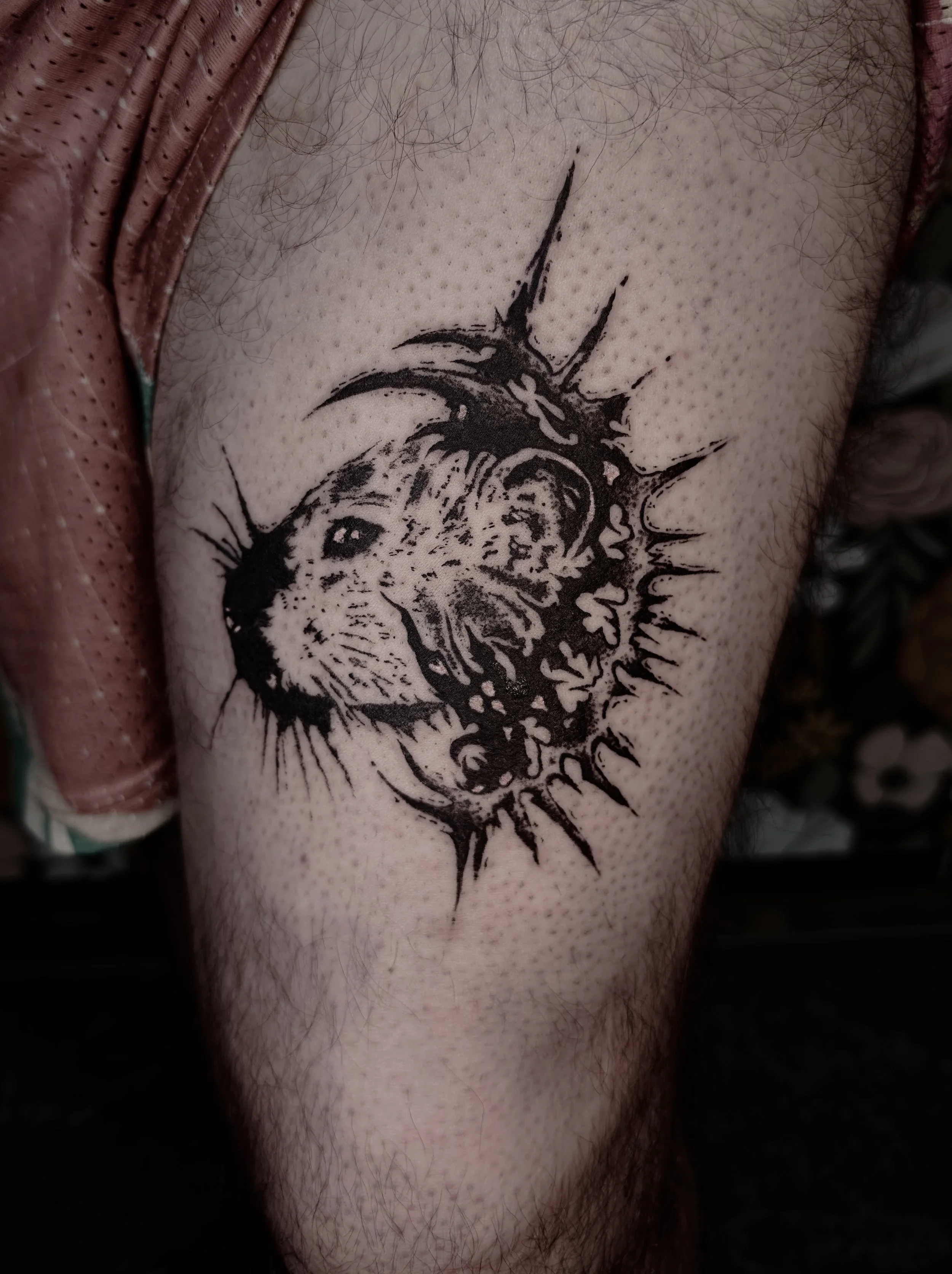 Tattoo of a roaring lion's face with abstract, jagged lines resembling a sunburst or explosion around the head. Cybersigilism rat face.