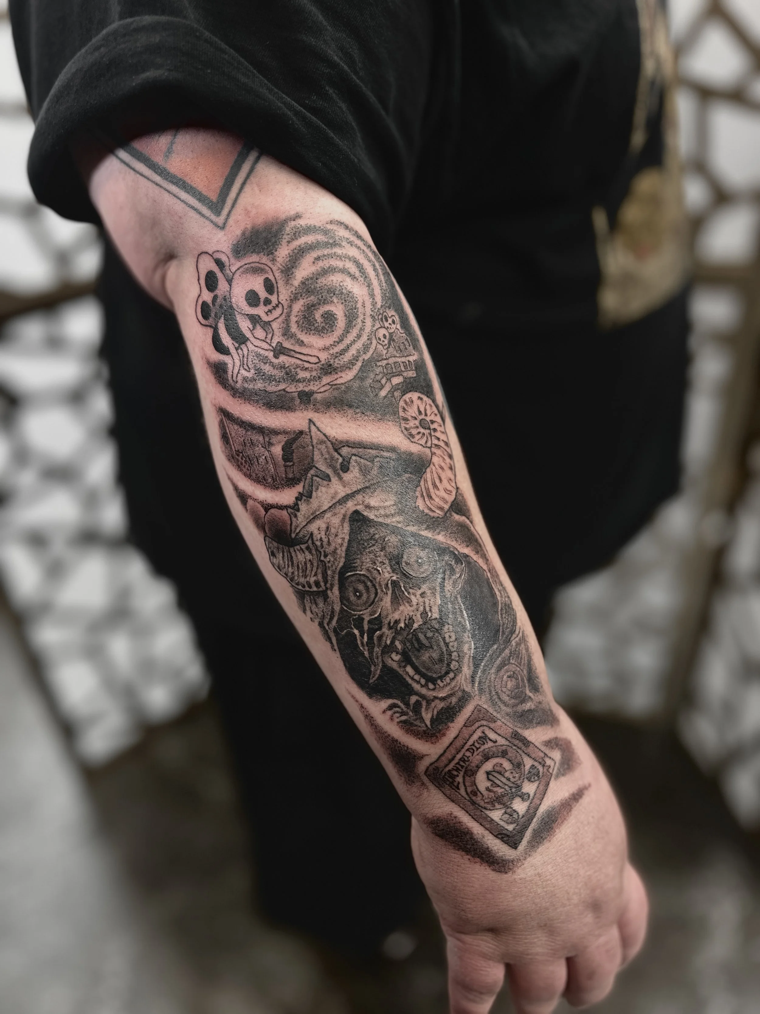 A detailed black and gray tattoo sleeve featuring the Lytch from Adventure Time with an exaggerated expression, a swirling vortex, and a playing card with a skeleton figure.