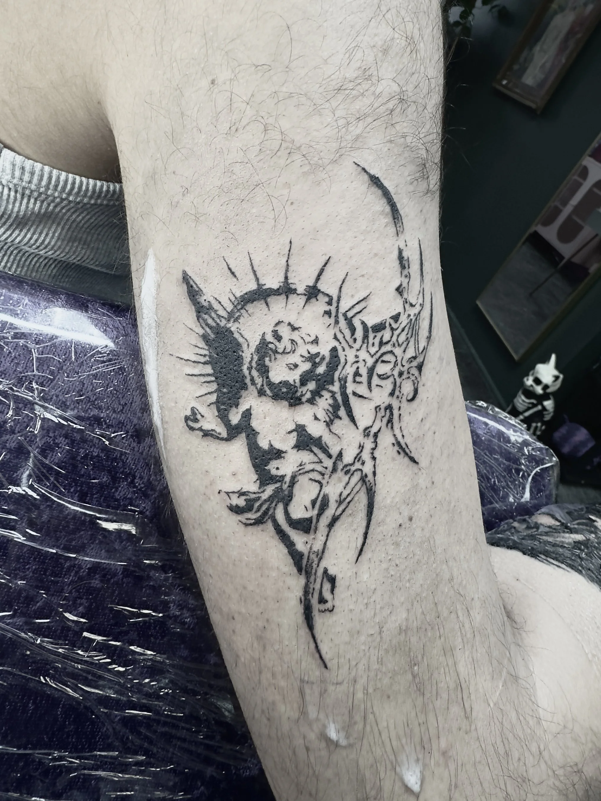A black ink cybersigilism tattoo of a cherub, positioned on a person's forearm.