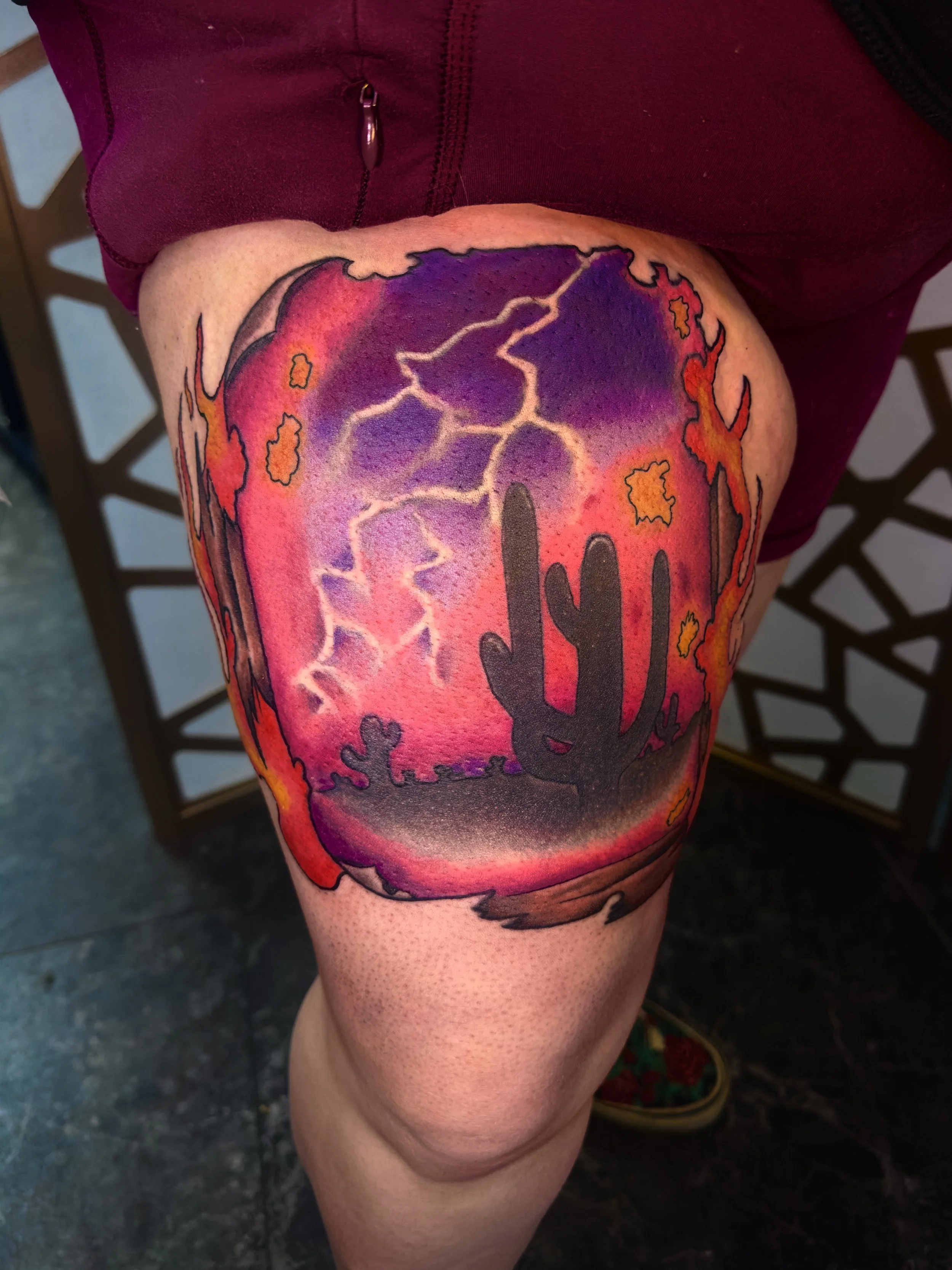 Colorful tattoo featuring a desert scene with a cactus, lightning, and vibrant sunset hues.
