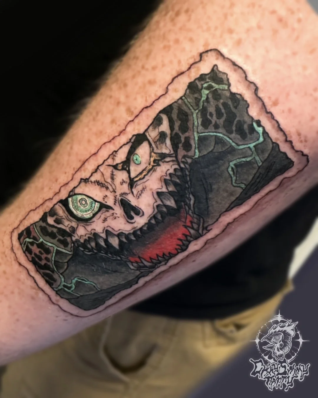 Tattoo of a Kafka from Kaiju NO.8 with sharp teeth and detailed scales, featuring green eyes and dark coloring, on a person's arm.