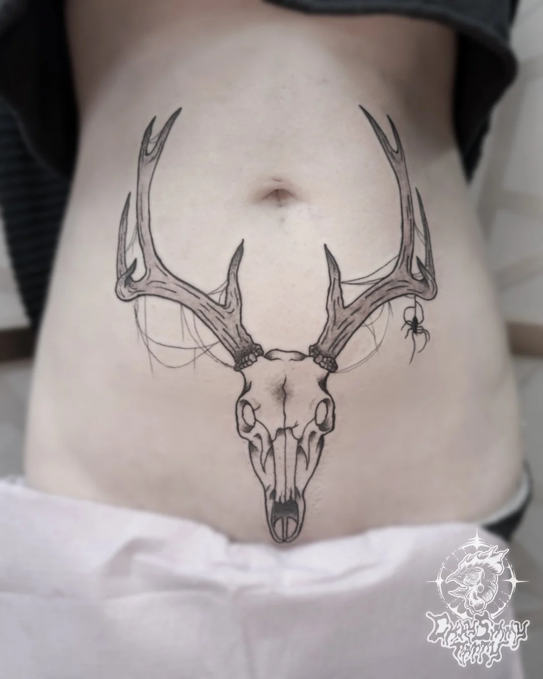 Tattoo of a deer skull with antlers on a person's lower abdomen.
