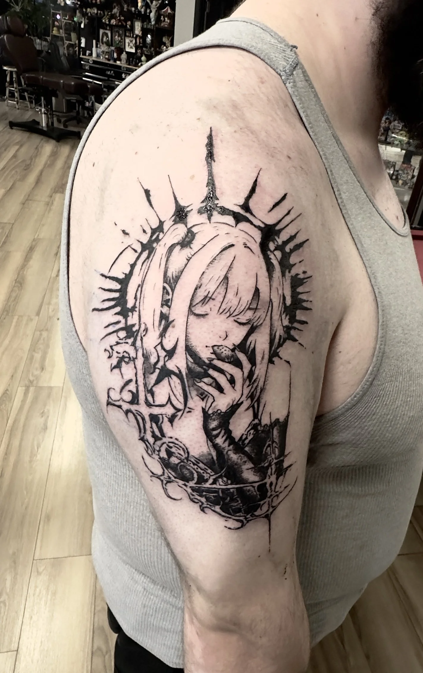 Black ink tattoo of a girl with long hair holding a small object on her hand, surrounded by abstract, spiky designs on upper arm. Misa Amine from Death Note in cybersigilism 