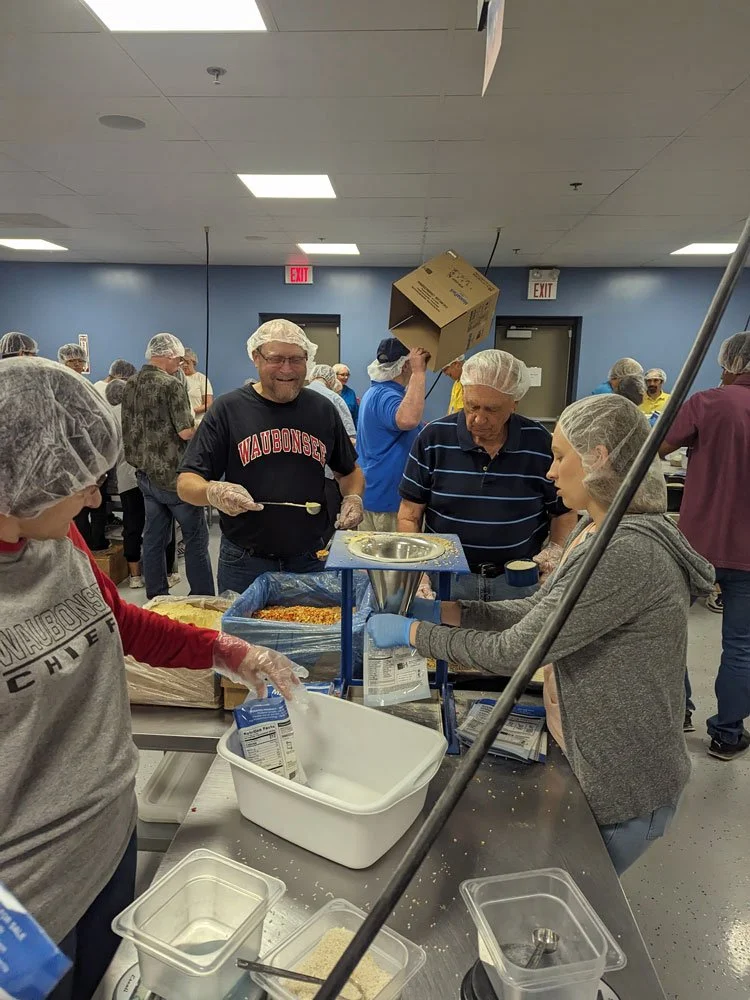 People in hairnets working together to package food at a volunteer event in a community center.