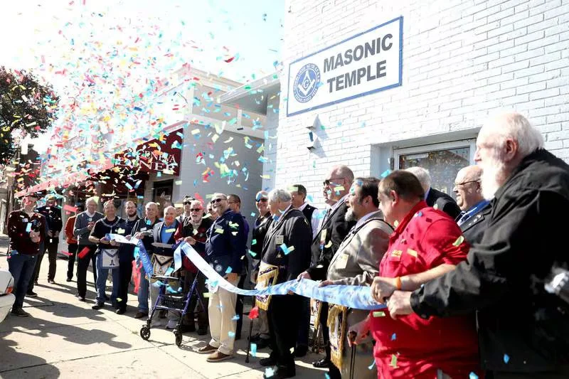 Masonic Temple ribbon cutting ceremony with people in attendance, confetti in the air, and a sign that reads 'Masonic Temple'