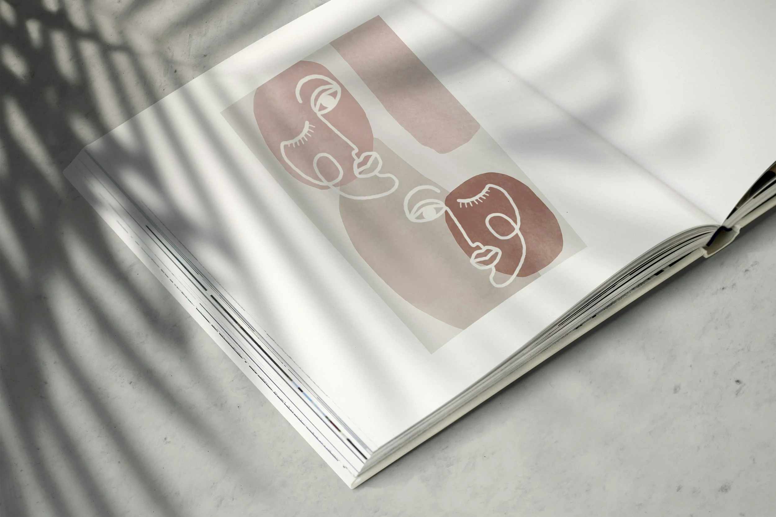 Open book with abstract line art faces in pink and white, with shadows falling across the pages, on a light-colored surface.