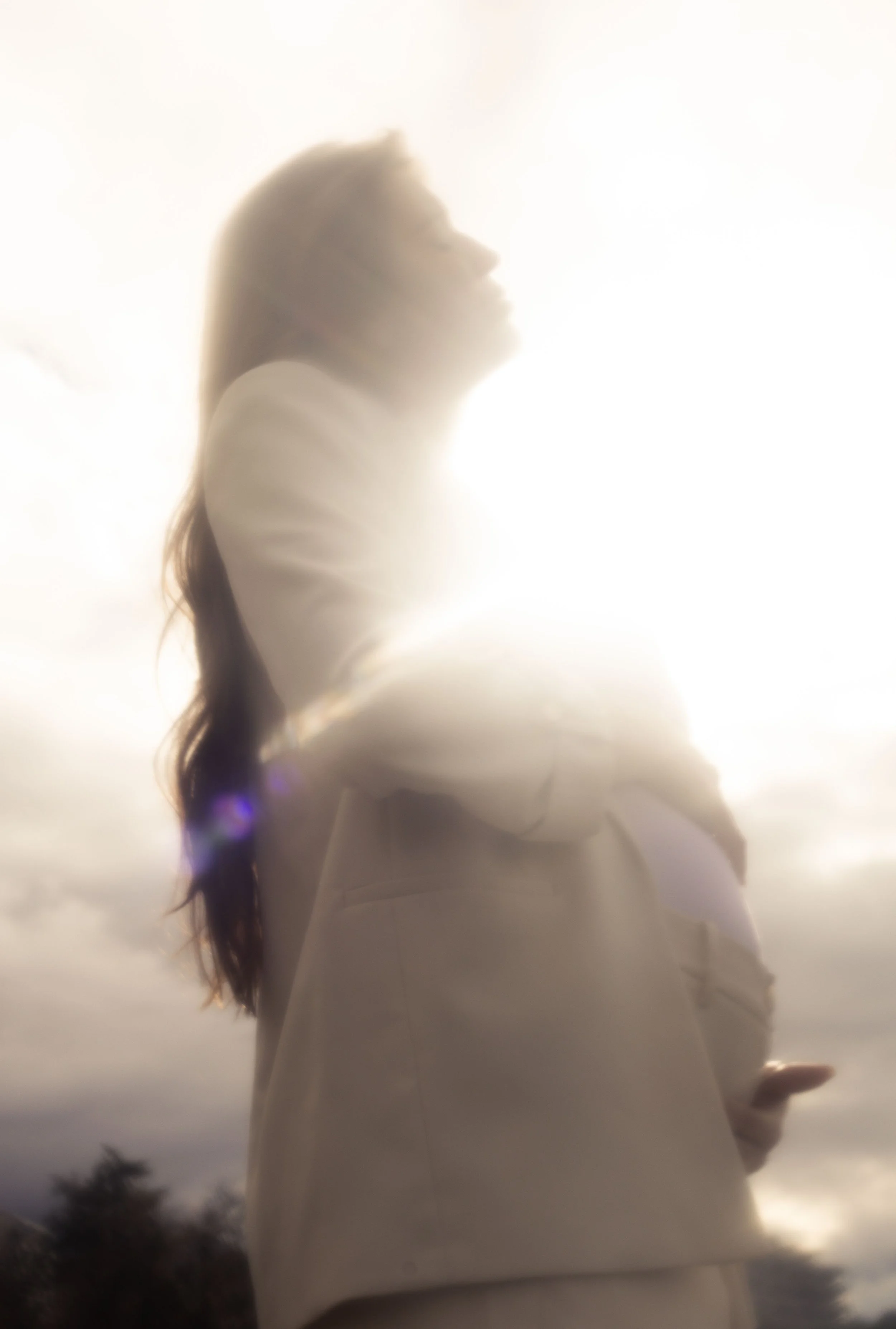 Une femme regarde vers le ciel, éclairée par la lumière du soleil derrière elle, créant un effet de halo brillant.