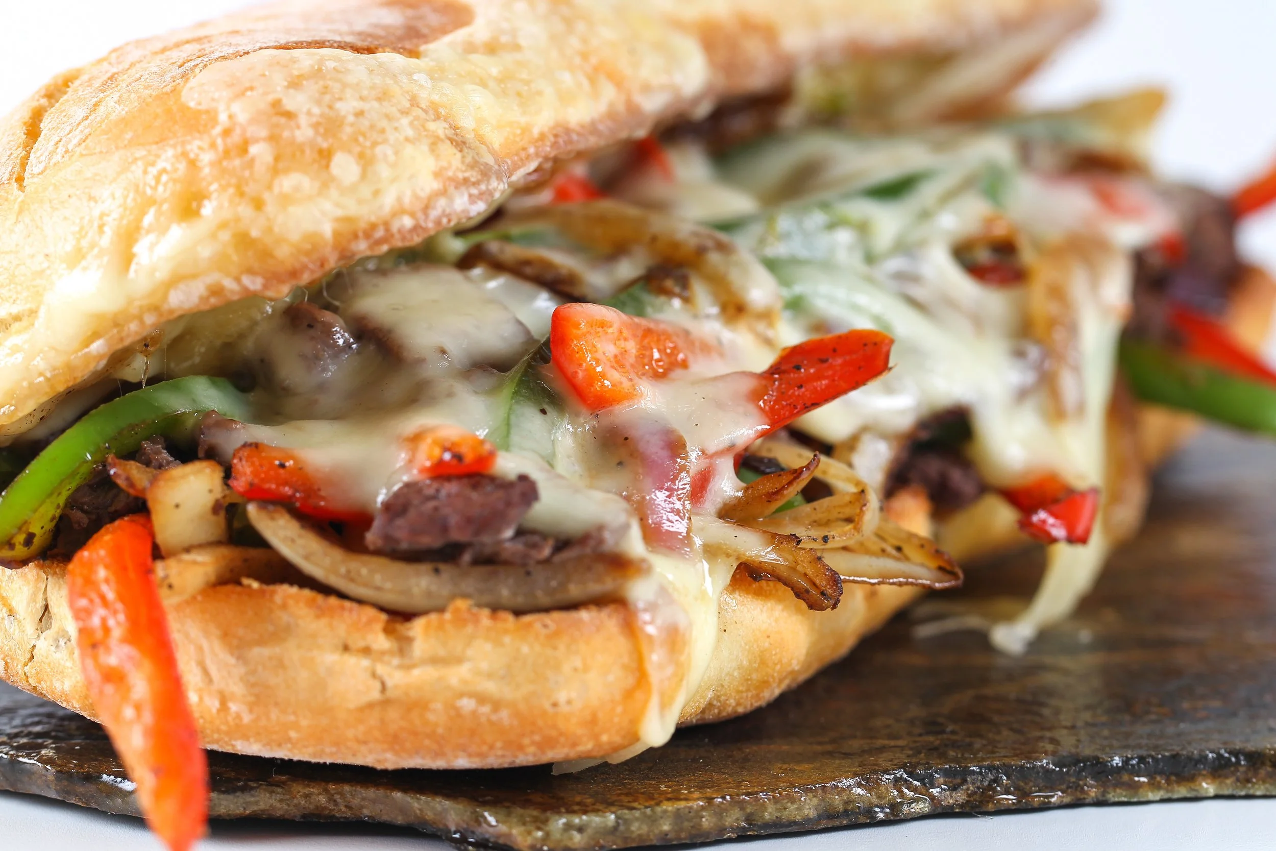 Close-up of a sandwich with melted cheese, beef, green and red peppers, onions, and a toasted bun.