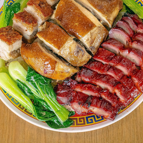 Assorted Asian-style cooked meats with green leafy vegetables on a decorative plate.