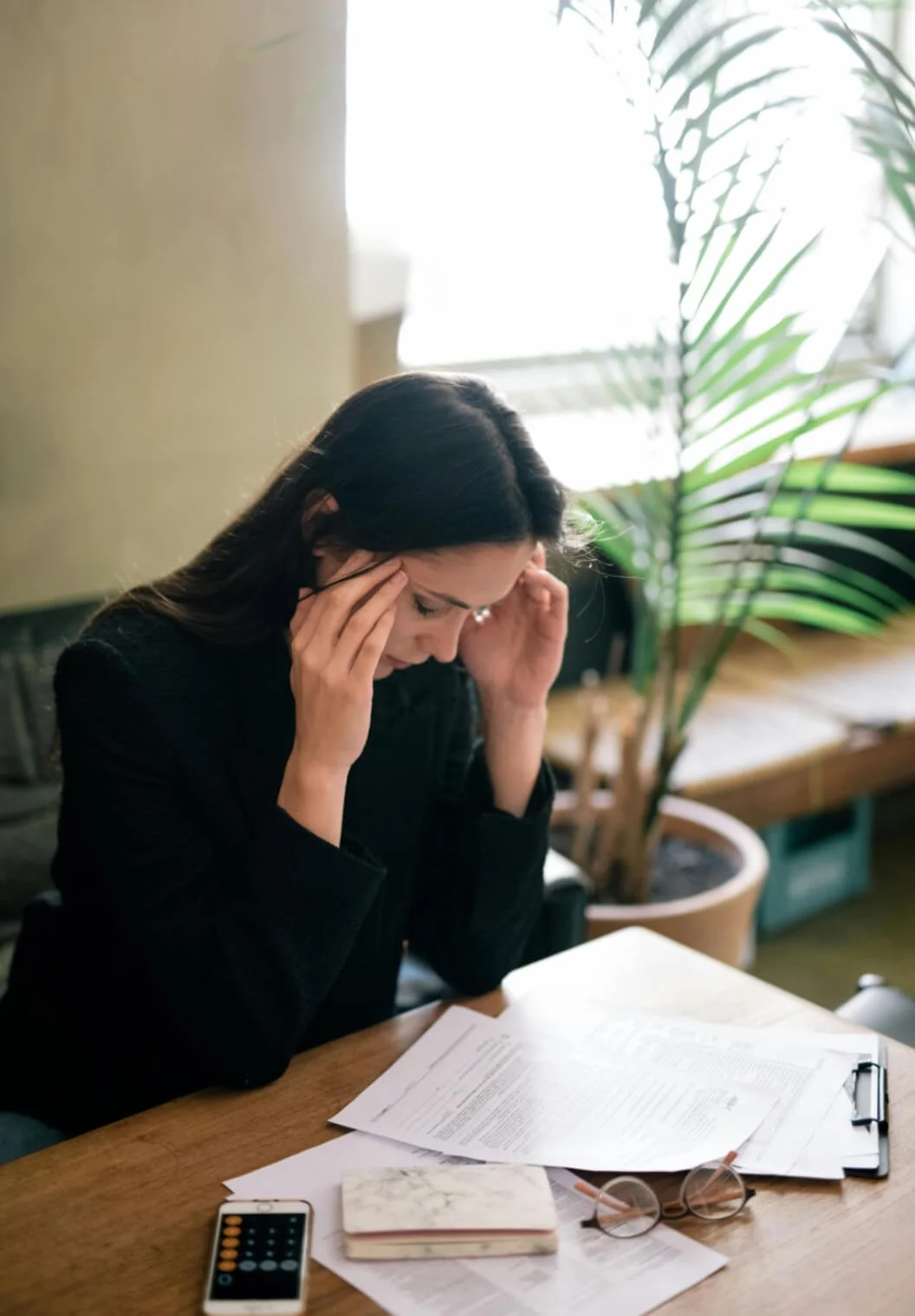 A stressed out woman holding her temples, while looking at bills and paperwork
