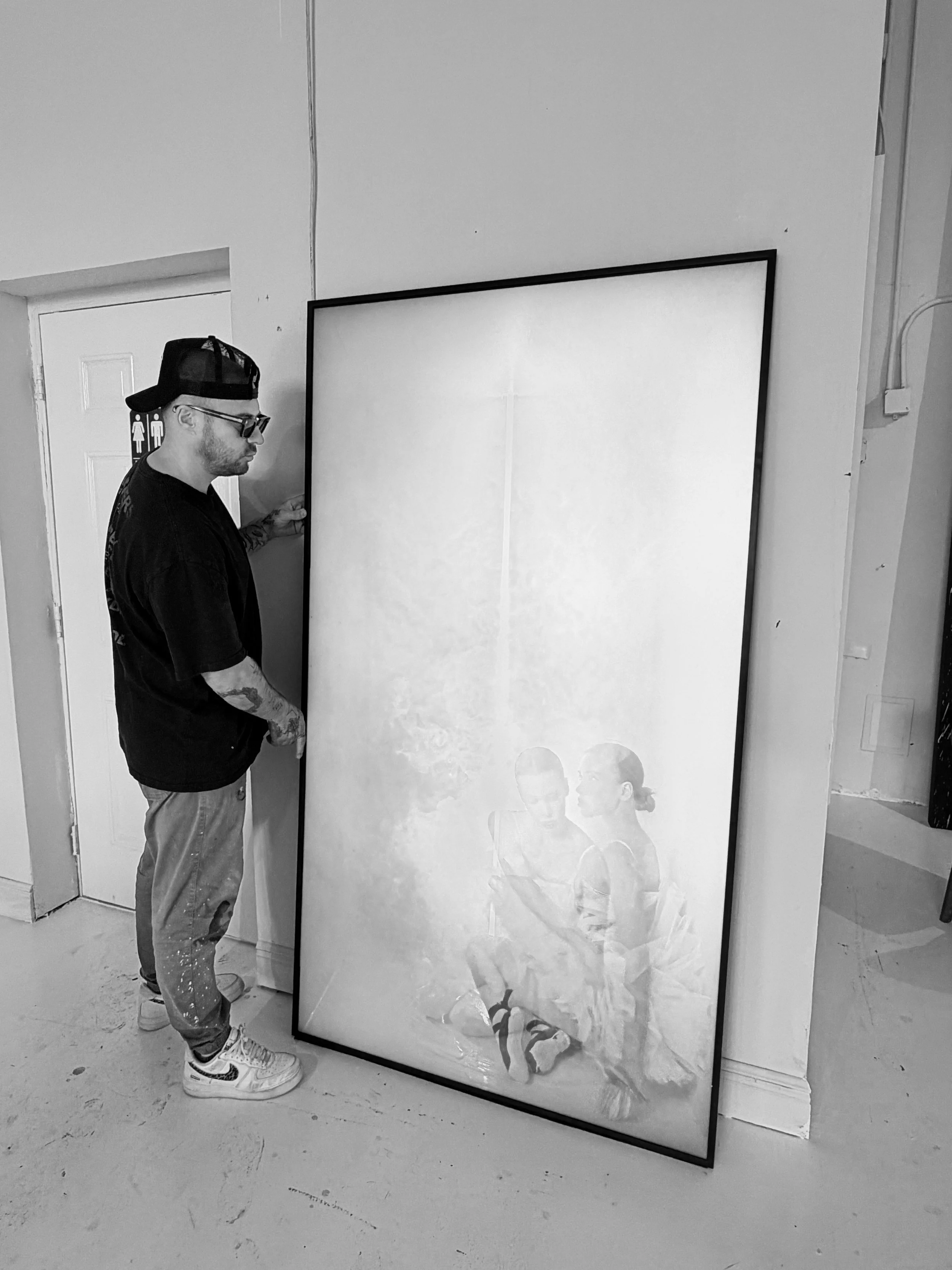 Artist Roman Lefebvre standing beside a large framed photographic artwork in the studio.