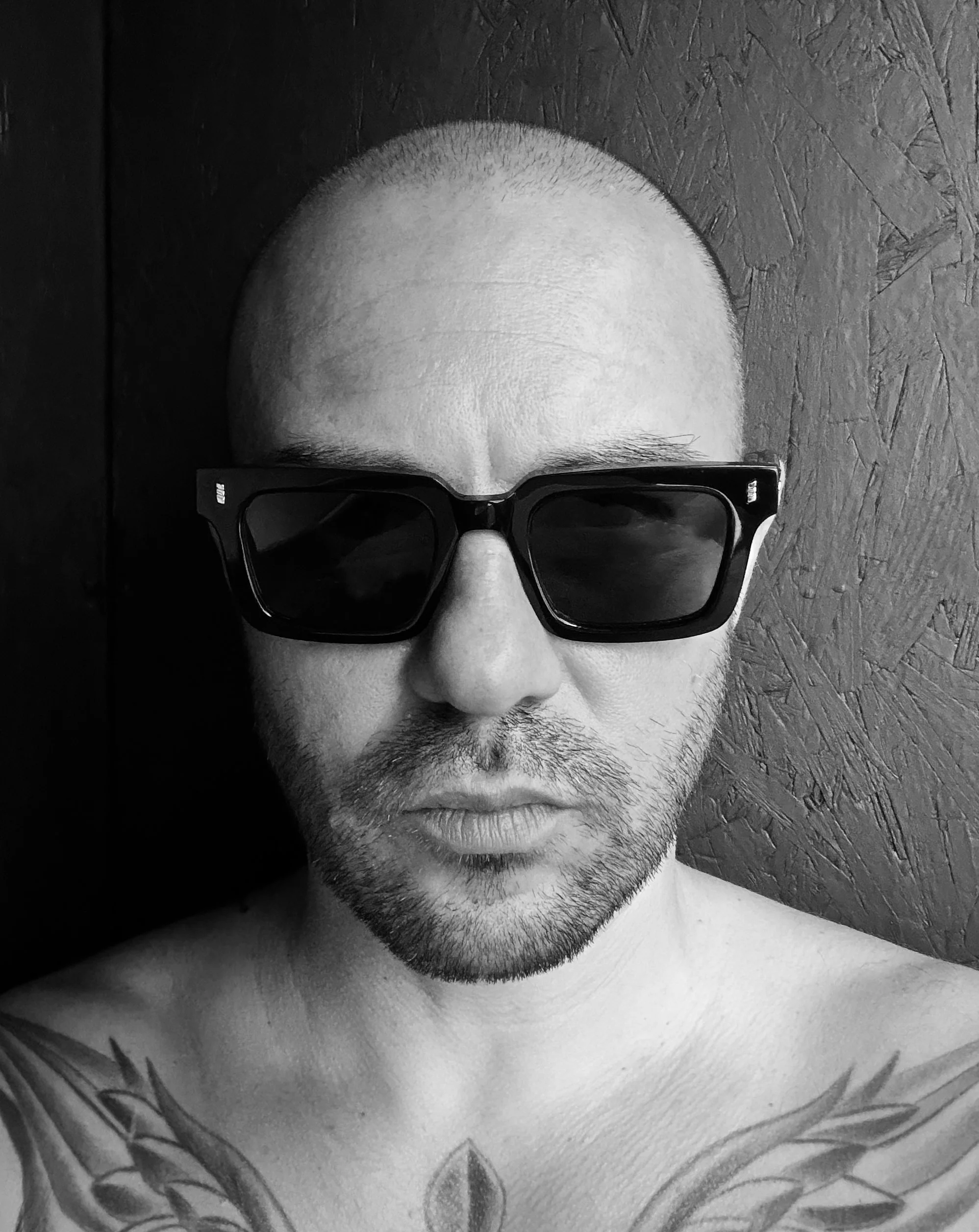 Portrait of artist Romain Lefebvre in black and white, wearing sunglasses against a textured wall.