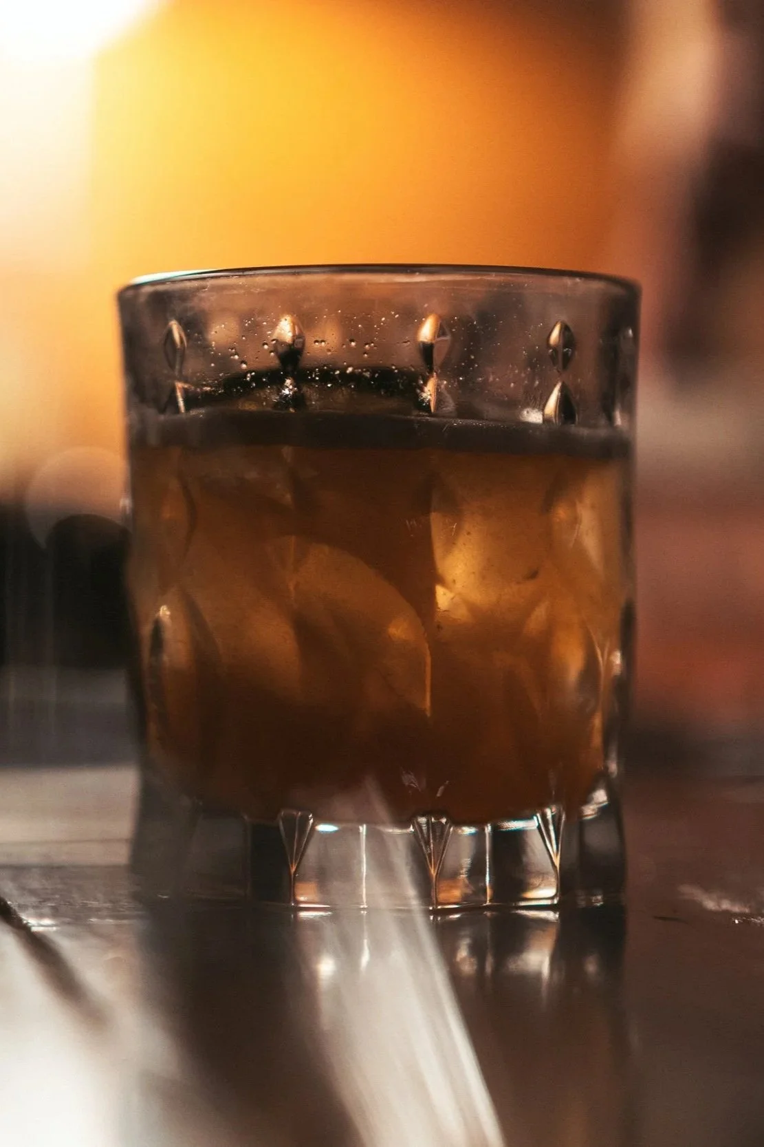A close-up of a glass filled with a dark beverage, possibly soda or whiskey, with ice cubes inside, placed on a wooden surface.